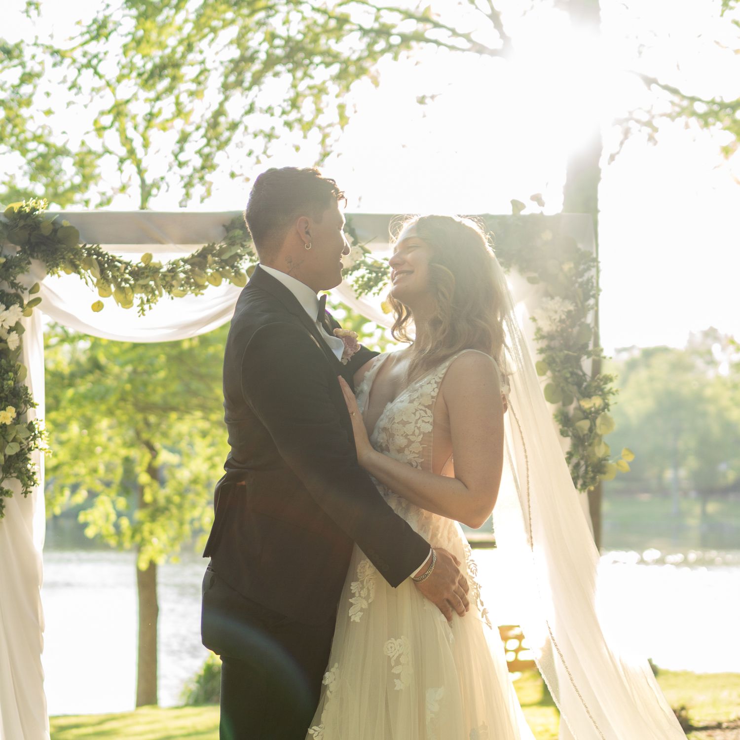A romantic sunset wedding portrait with golden light filtering through trees and white draping.