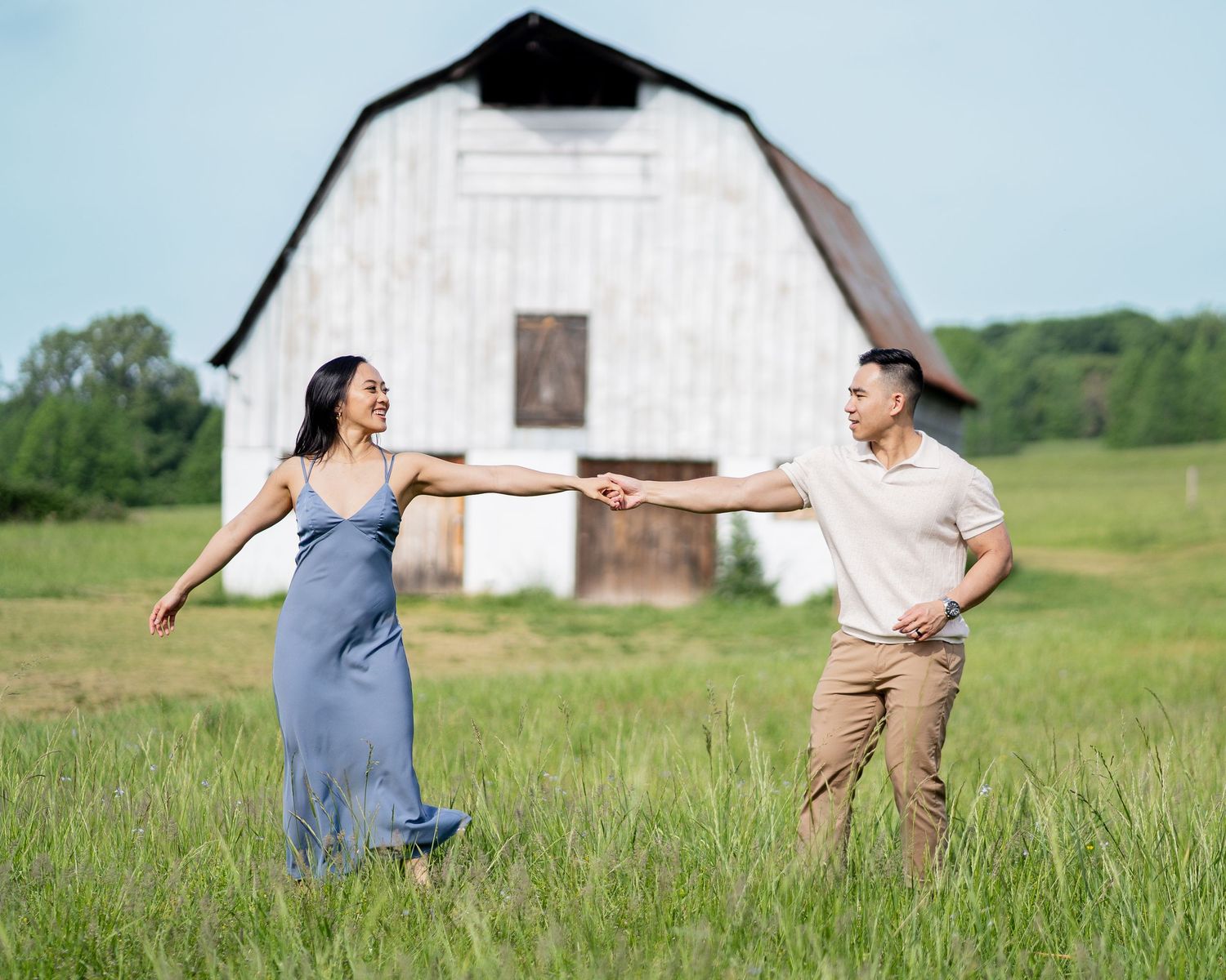 Two people dance and twirl in a field with a rustic barn in the background.