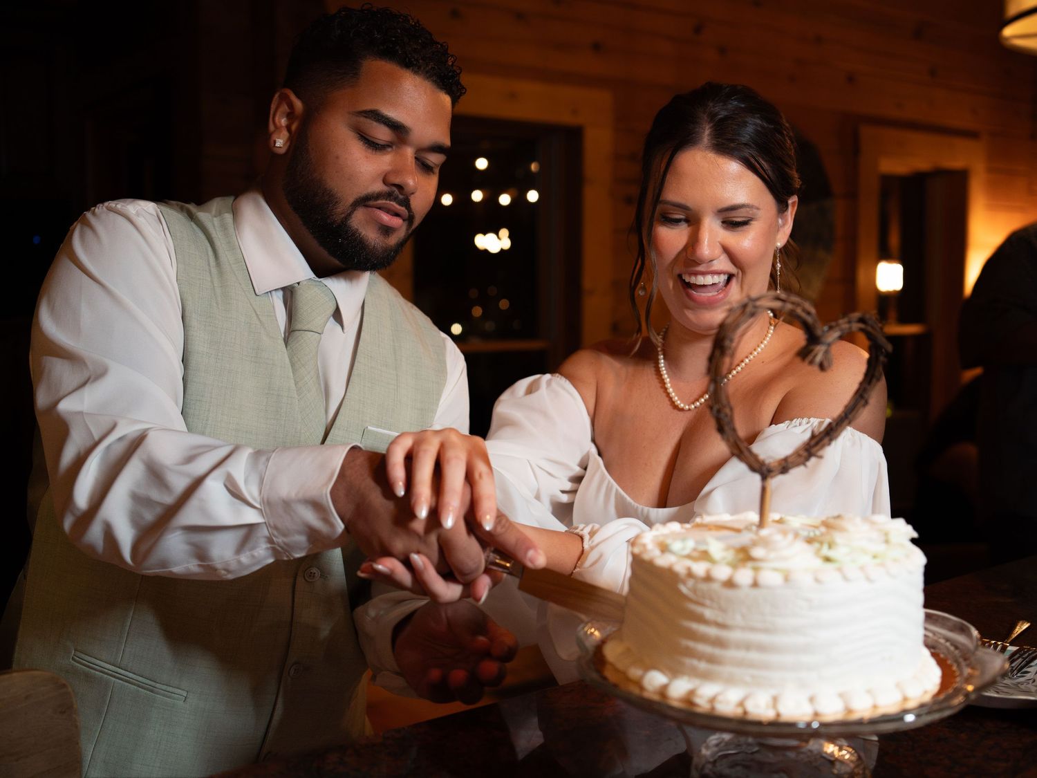 A couple cutting their white wedding cake together during their reception celebration.