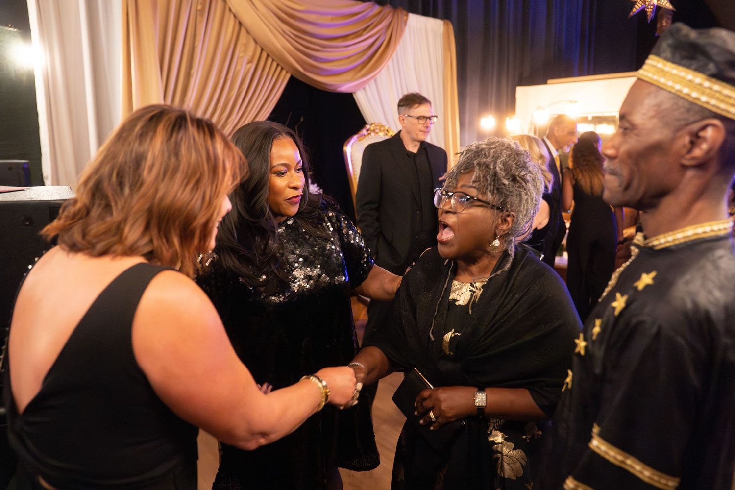 Elegantly dressed guests mingling and shaking hands at a formal evening gala event.