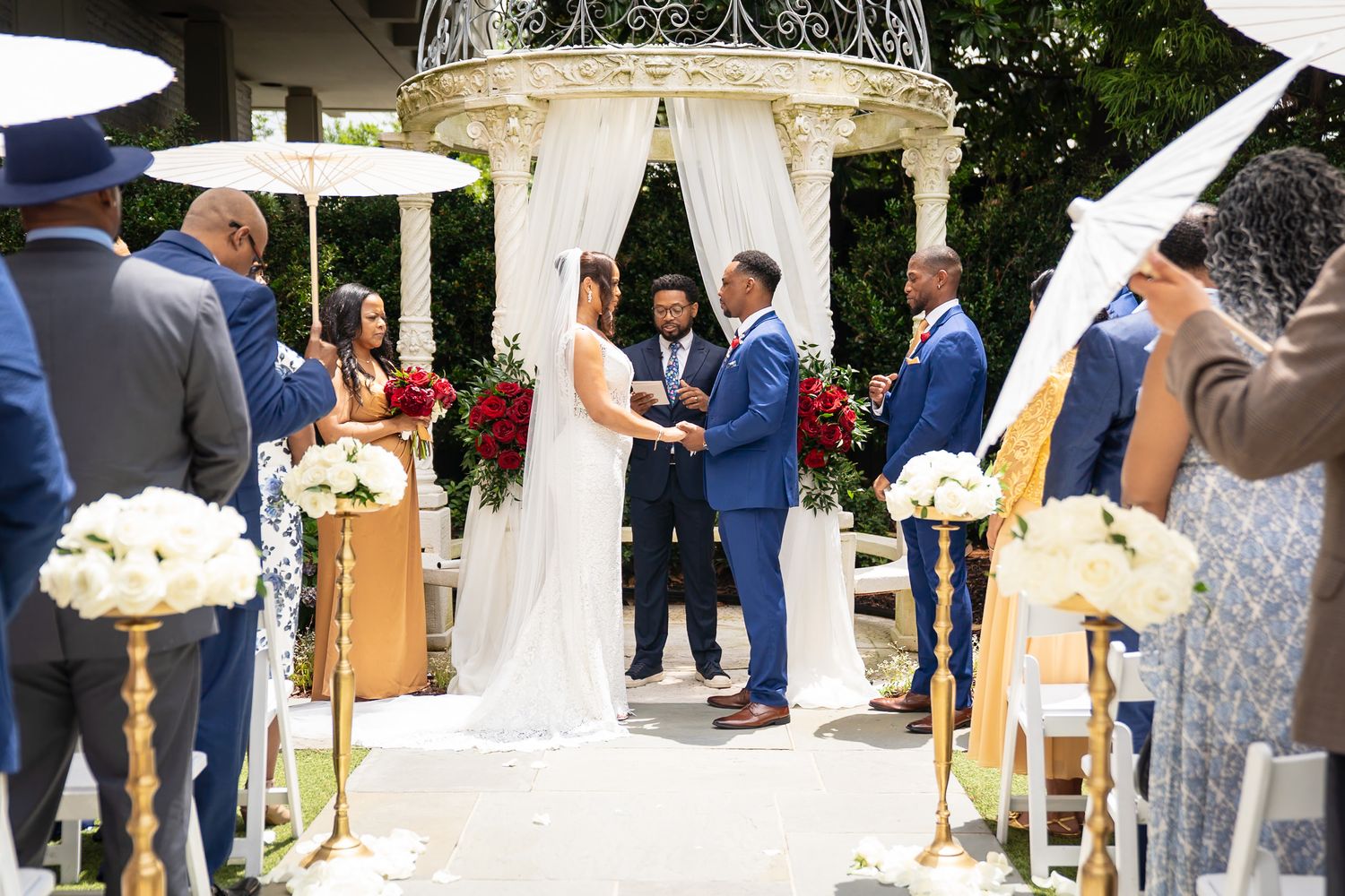 Outdoor wedding ceremony setup with white chairs and floral arrangements in a garden setting.