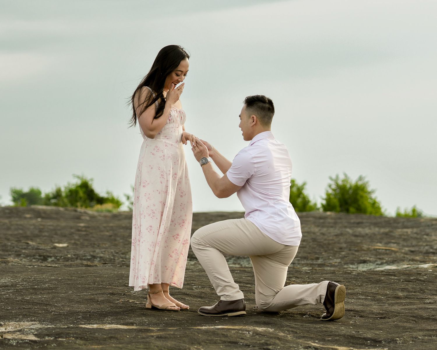 Romantic proposal scene on a rocky beach during overcast weather.