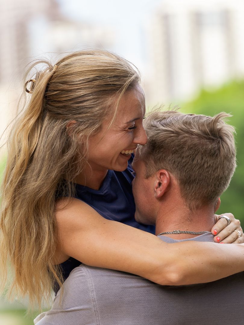 A joyful couple embracing and laughing outdoors, with the woman wrapping her arms around a man's neck.