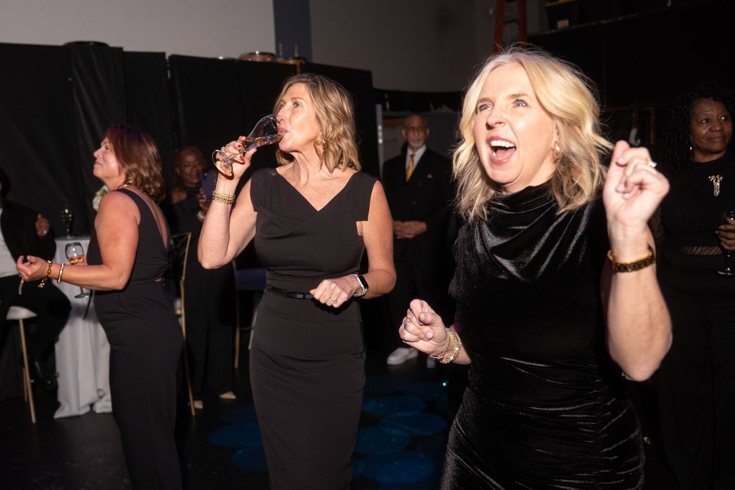 Women in black dresses dancing and celebrating at an elegant evening gala event.