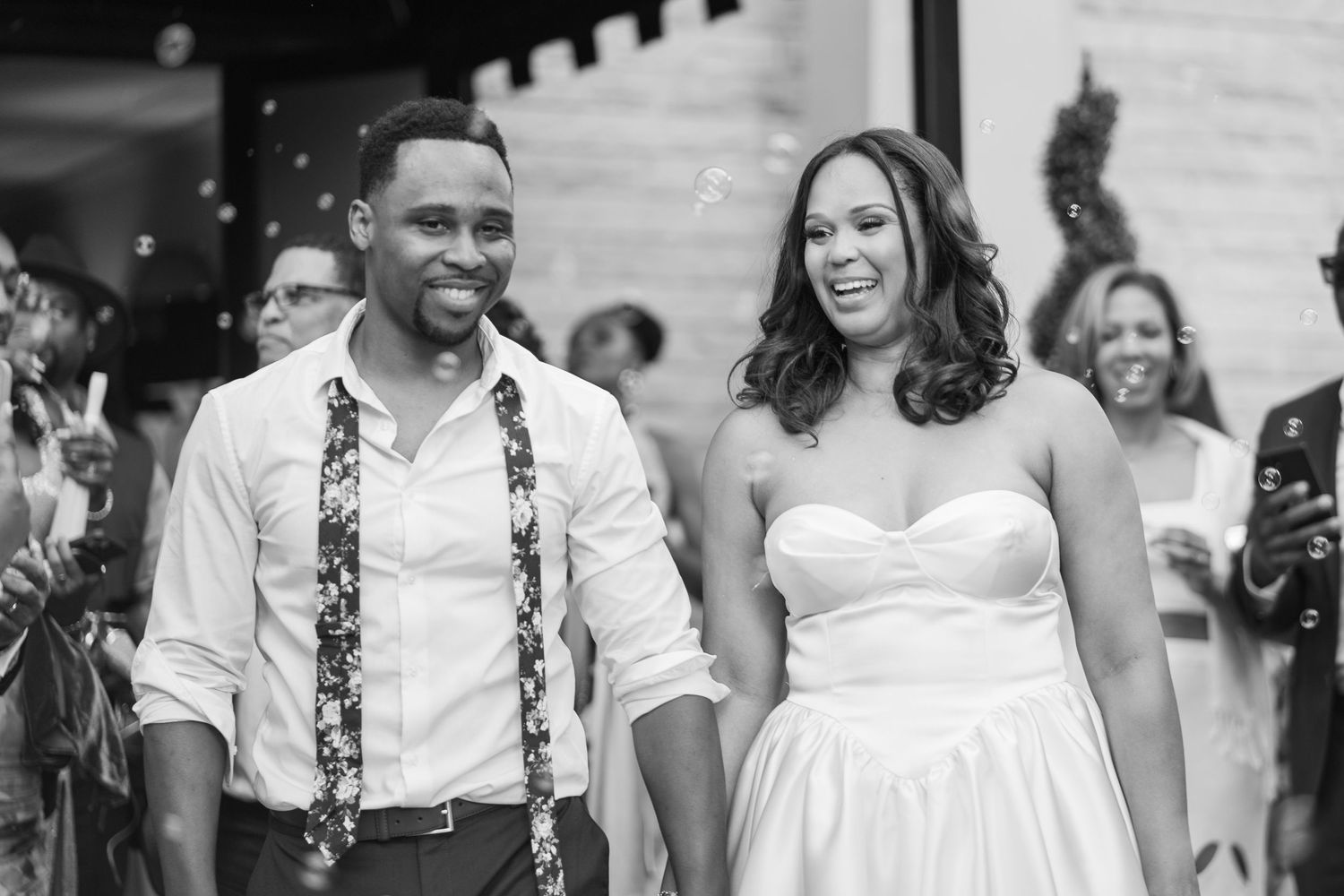 A happy couple exits their wedding ceremony while guests celebrate in the background.