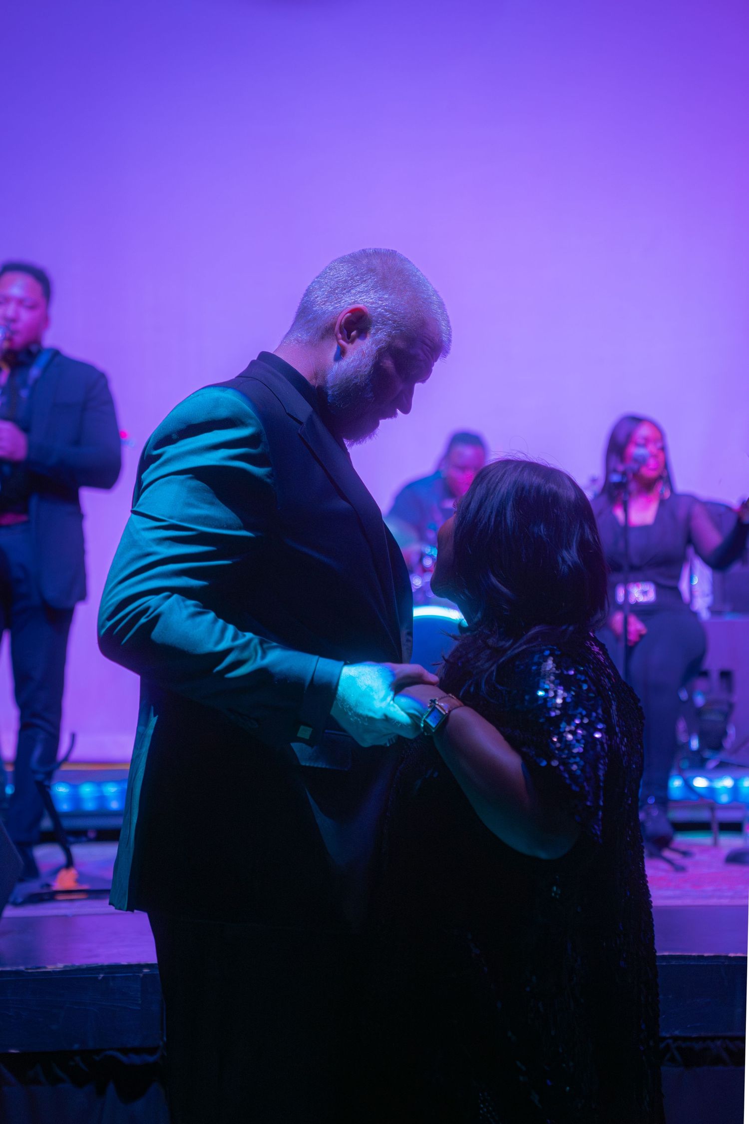 Couple sharing a romantic dance at a formal event with a live band performing on stage in purple lighting.