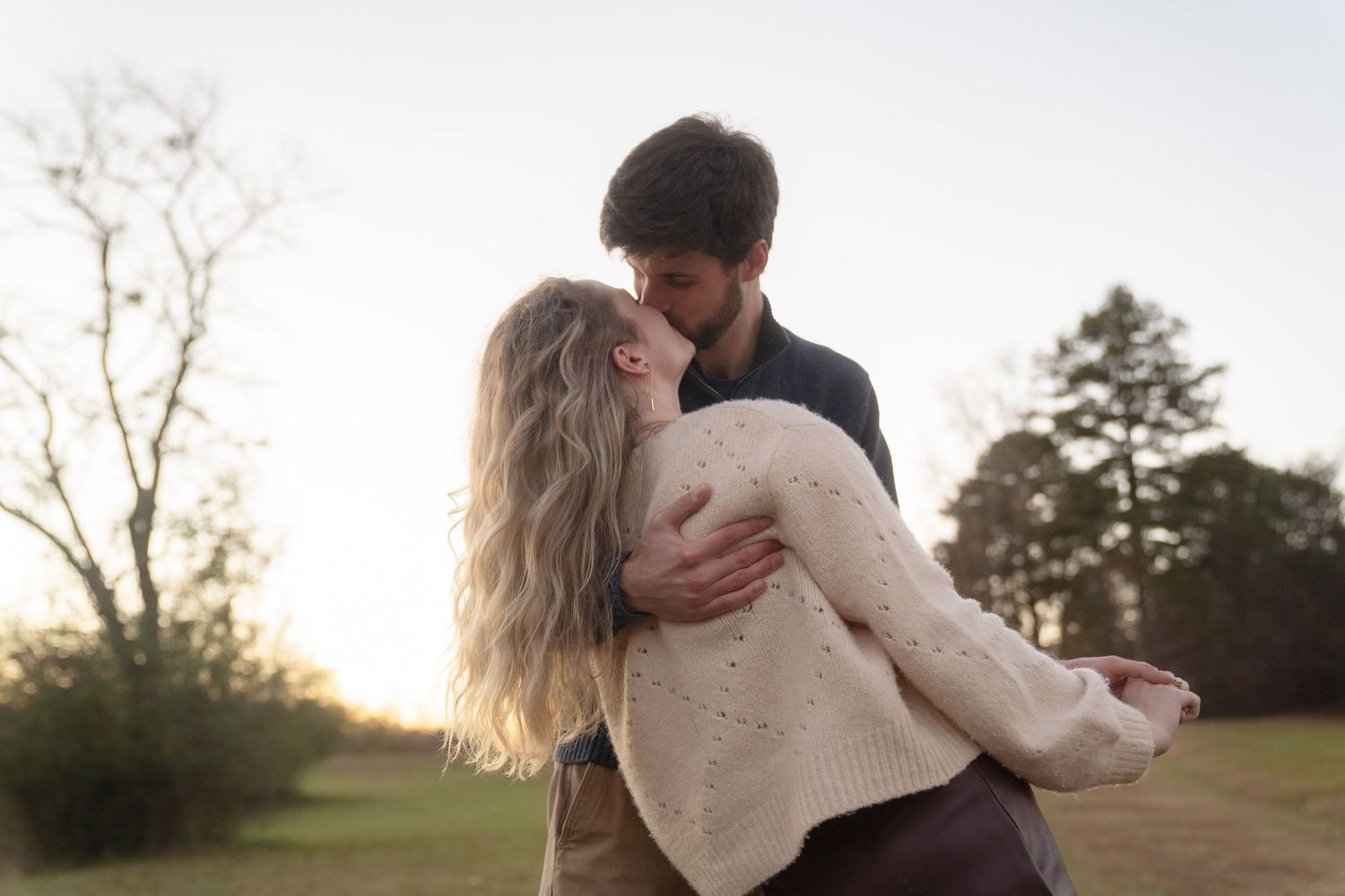 Romantic sunset engagement photo of a couple embracing outdoors in a natural field setting.
