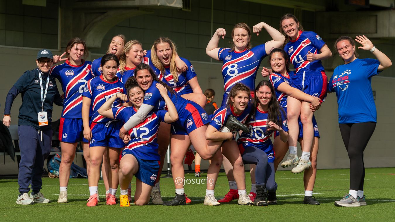 Women's AFL team celebrating in blue and red uniforms on a football field, posing joyfully for a group photo.
