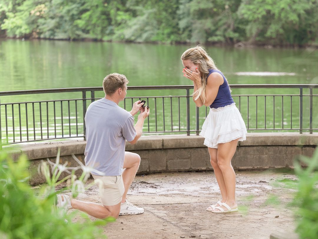 Proposal sequence by a lake with stone railing and lush greenery.