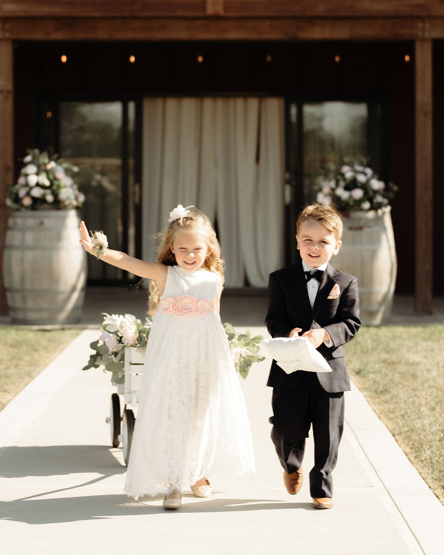 Flower girl and ring bearer walking joyfully down the aisle at an outdoor wedding.