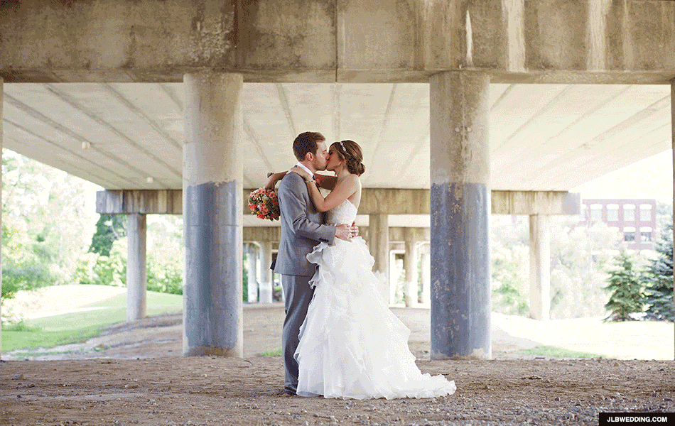 Bride and groom sharing a romantic kiss under a concrete bridge outdoors.