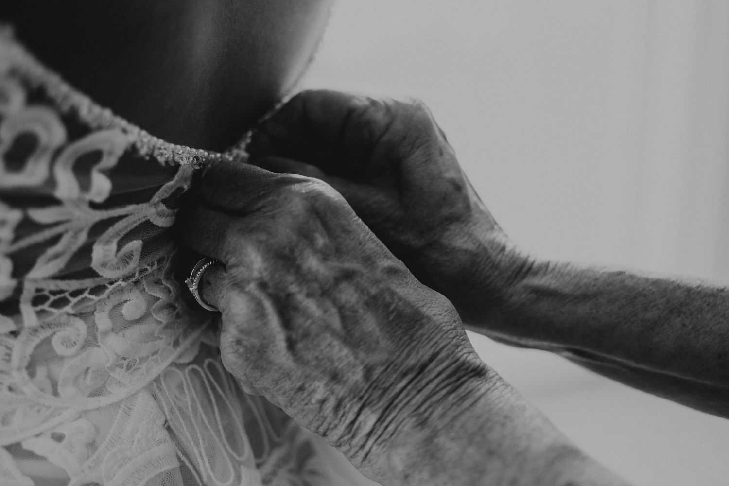 Black and white close-up of hands fastening the back of a lace wedding dress.