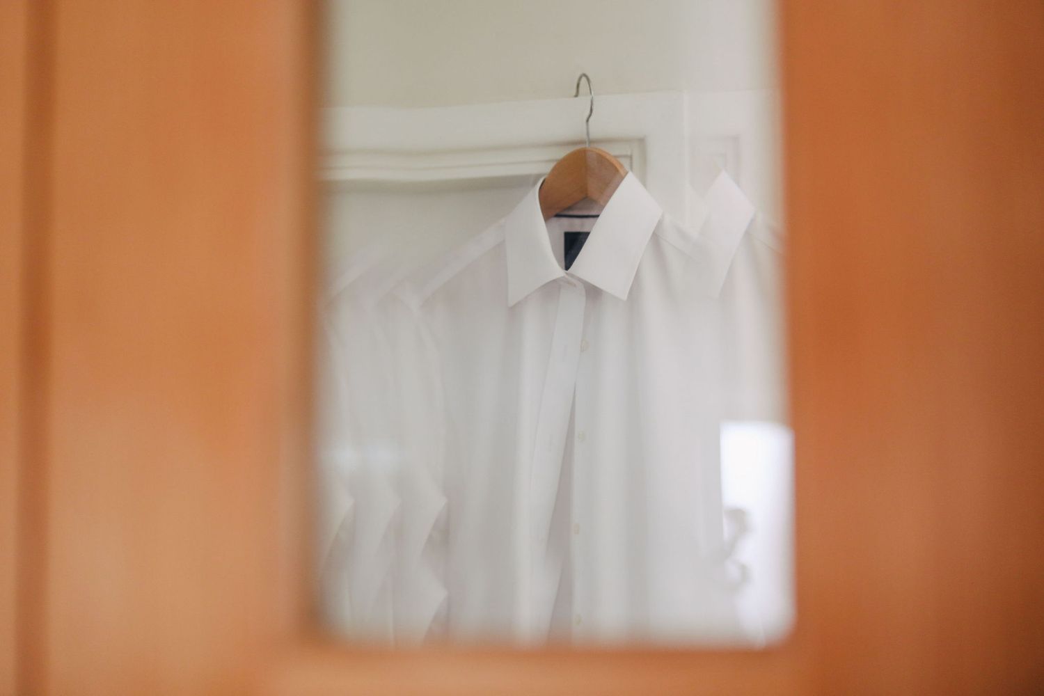 White dress shirt on a wooden hanger reflected in a mirror for a wedding preparation.