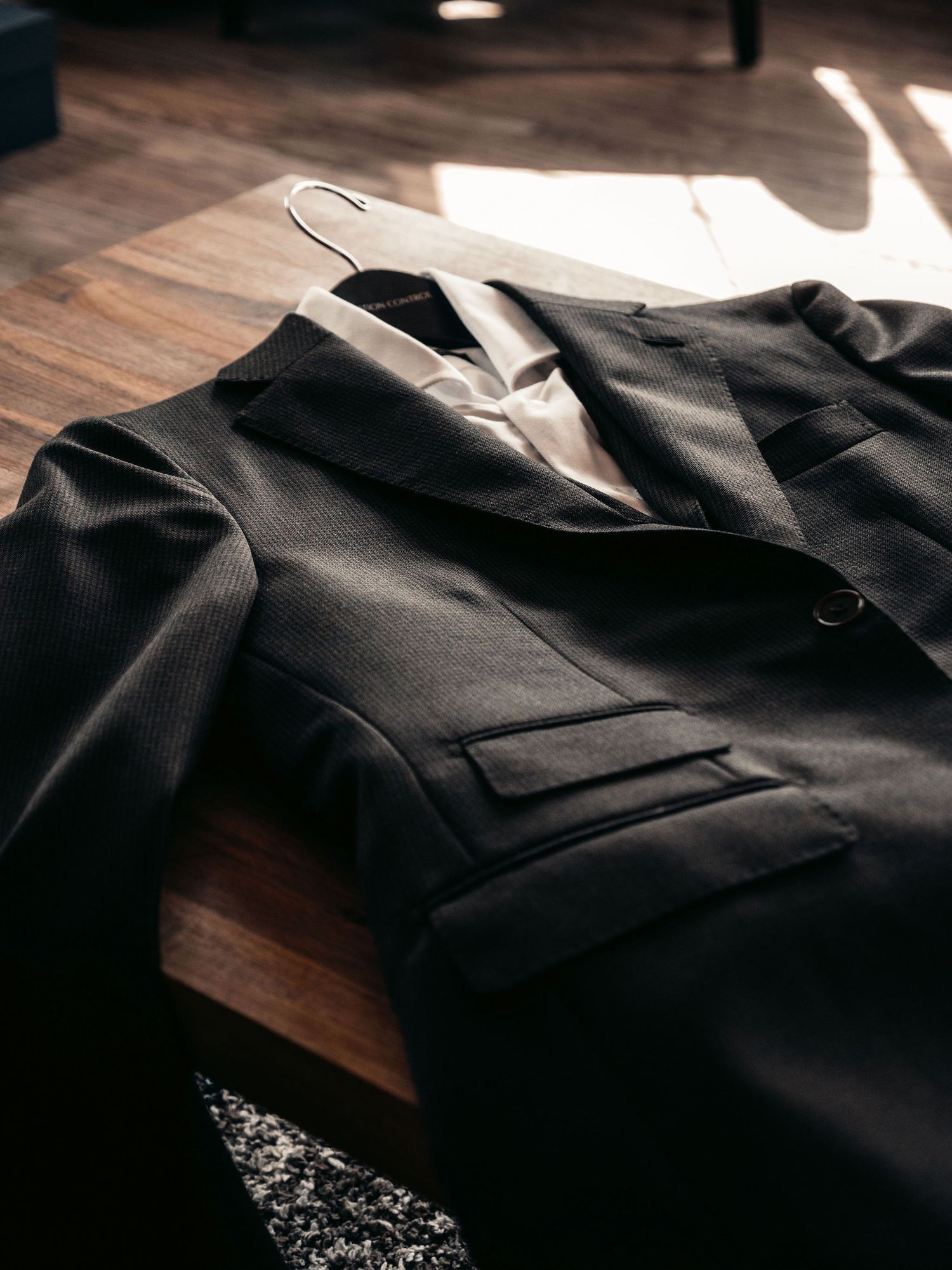 Dark suit jacket and trousers laid on a wooden surface in warm sunlight for a wedding.