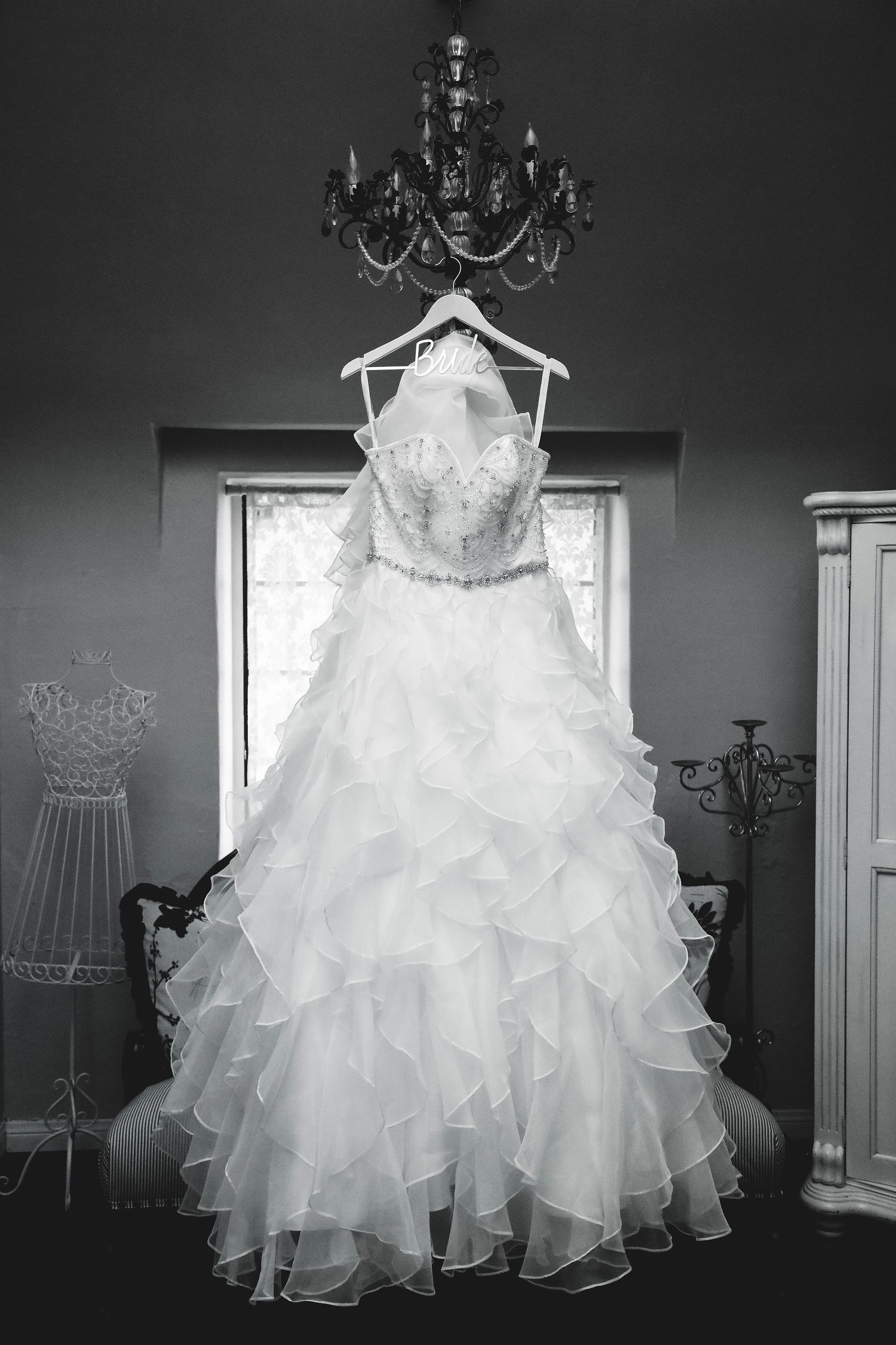 Black and white image of a ruffled ball gown wedding dress hanging from a chandelier.