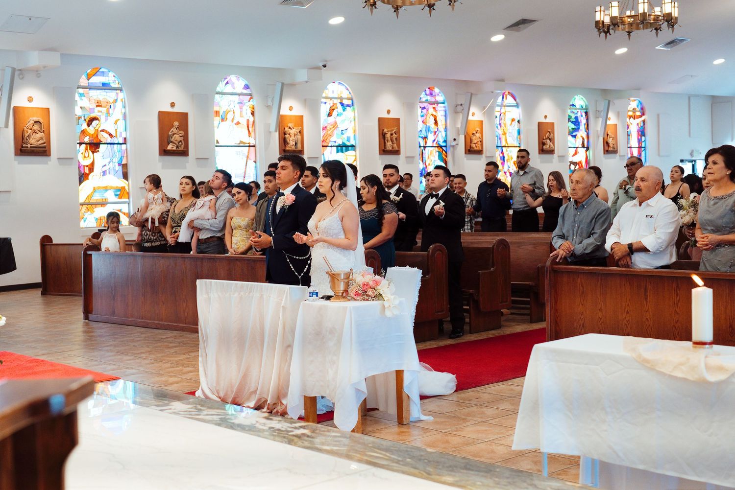 Bride and groom standing at the altar during a Catholic church wedding ceremony with guests seated in pews.