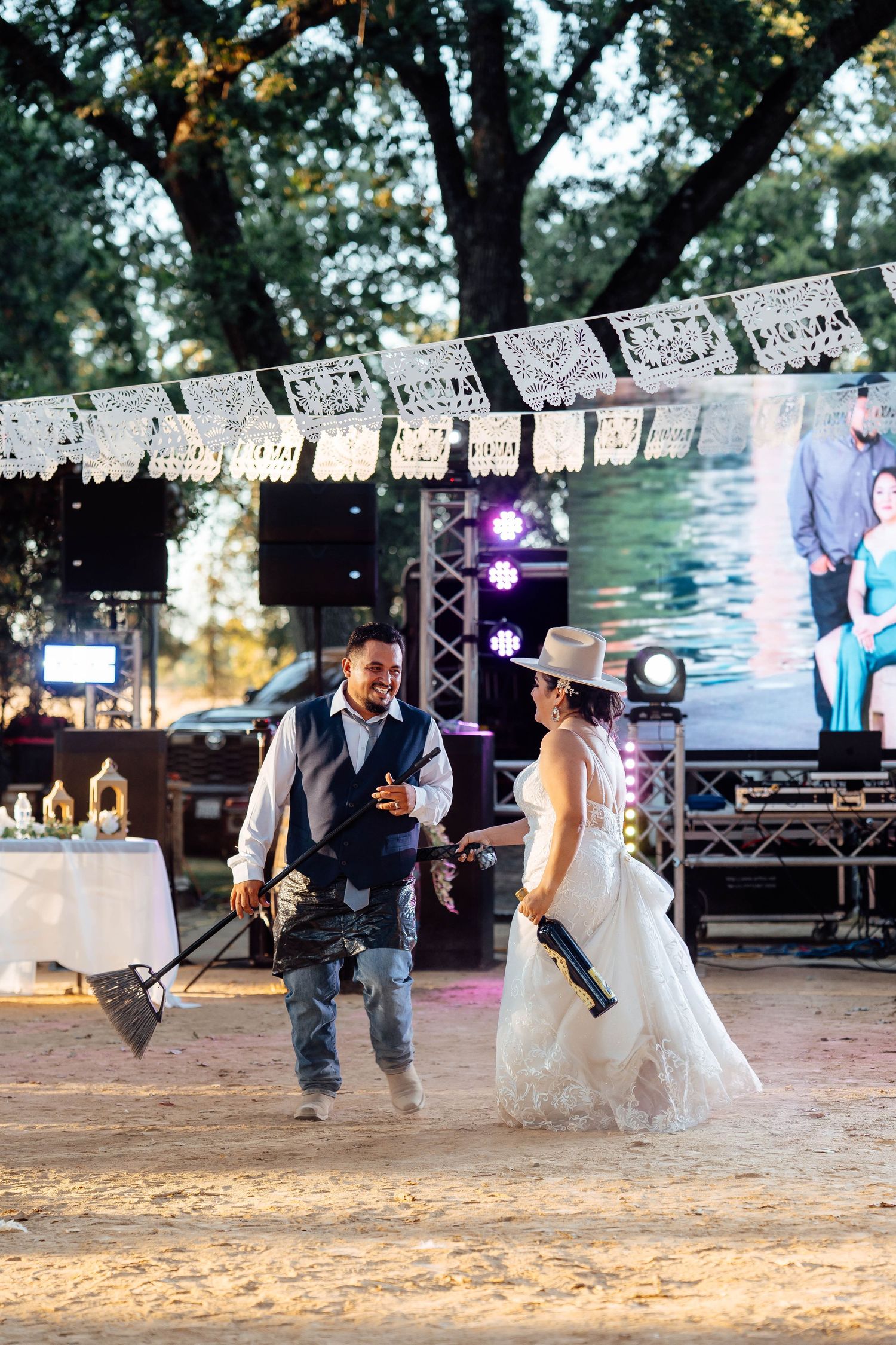 Bride and groom playfully holding toy guns at outdoor wedding reception with papel picado decorations.