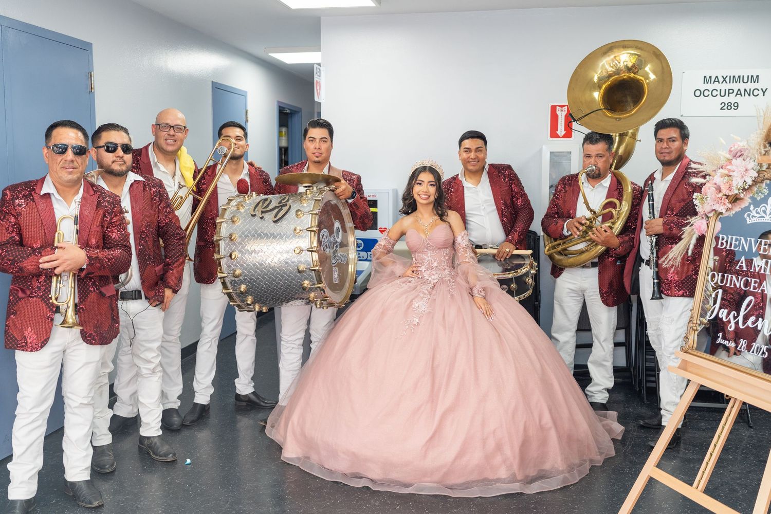 Quinceañera girl in pink ball gown poses with banda musicians in matching red jackets.