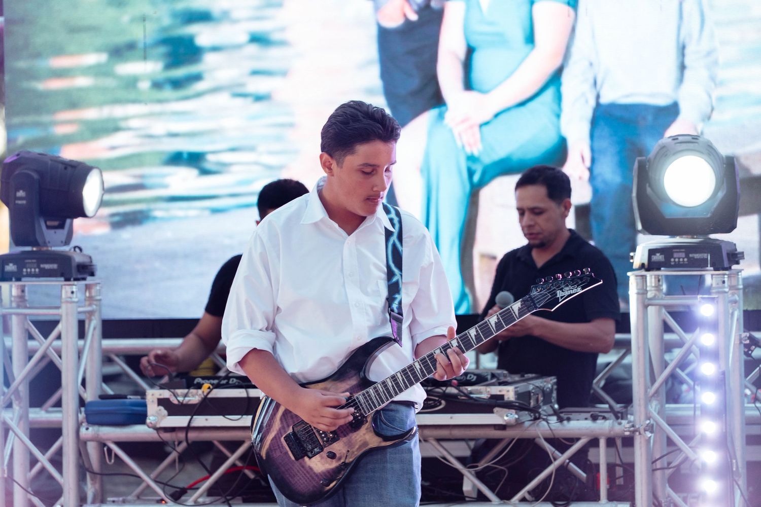 Musician playing electric guitar on stage at outdoor wedding reception with stage lighting.