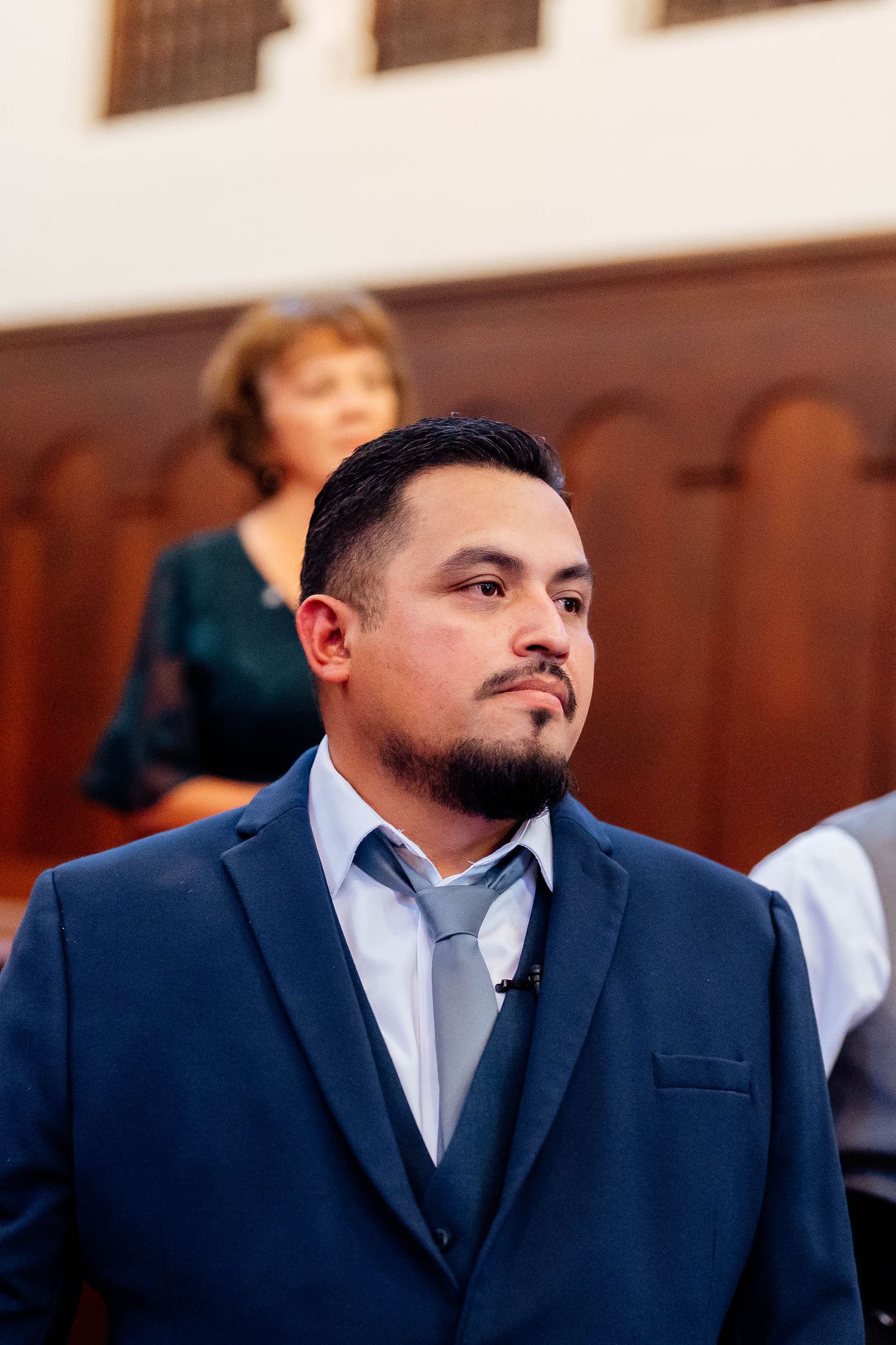 Groom in navy blue suit waits anxiously at altar during wedding ceremony.