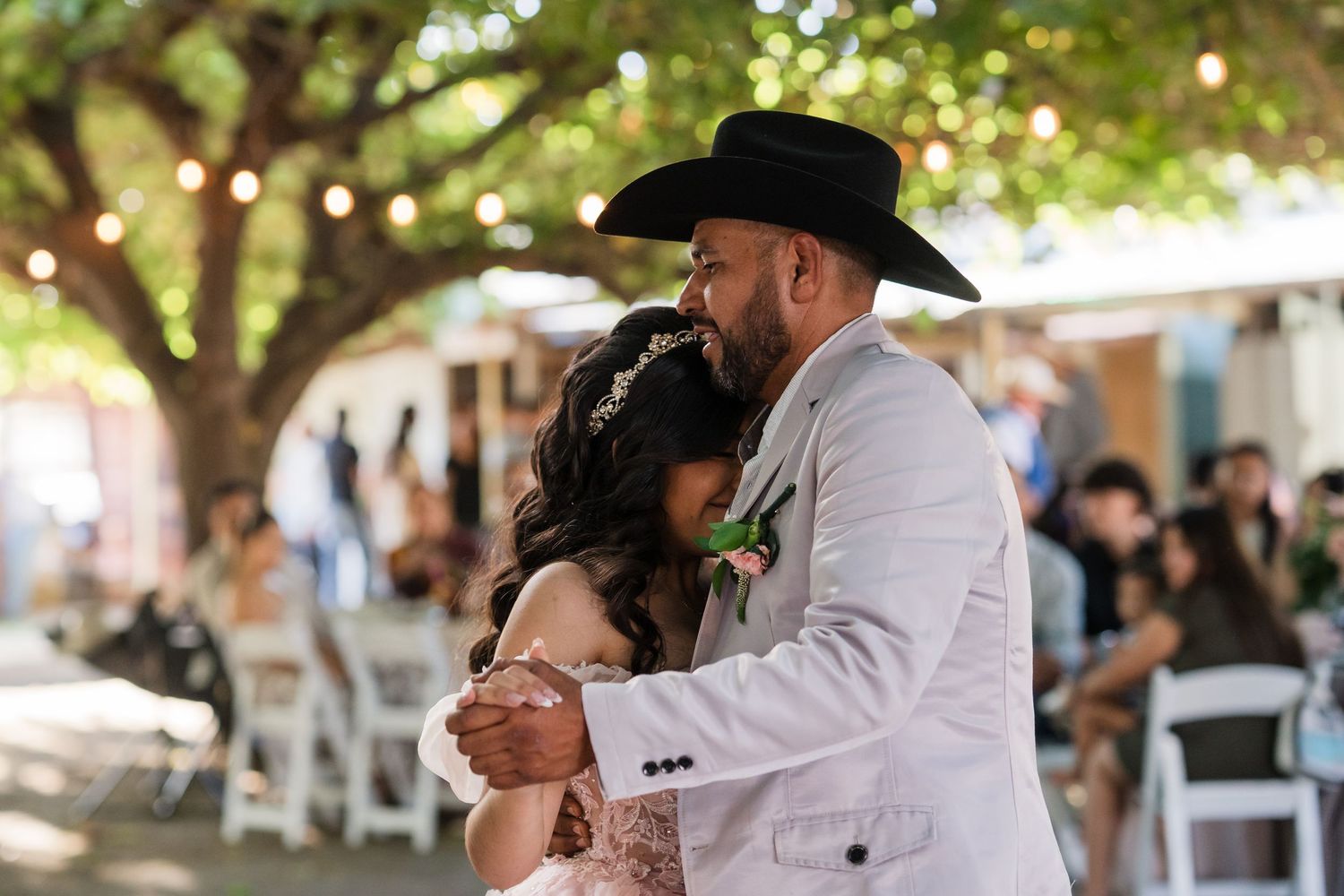 Bride and groom share first dance outdoors under trees with string lights at rustic wedding reception.
