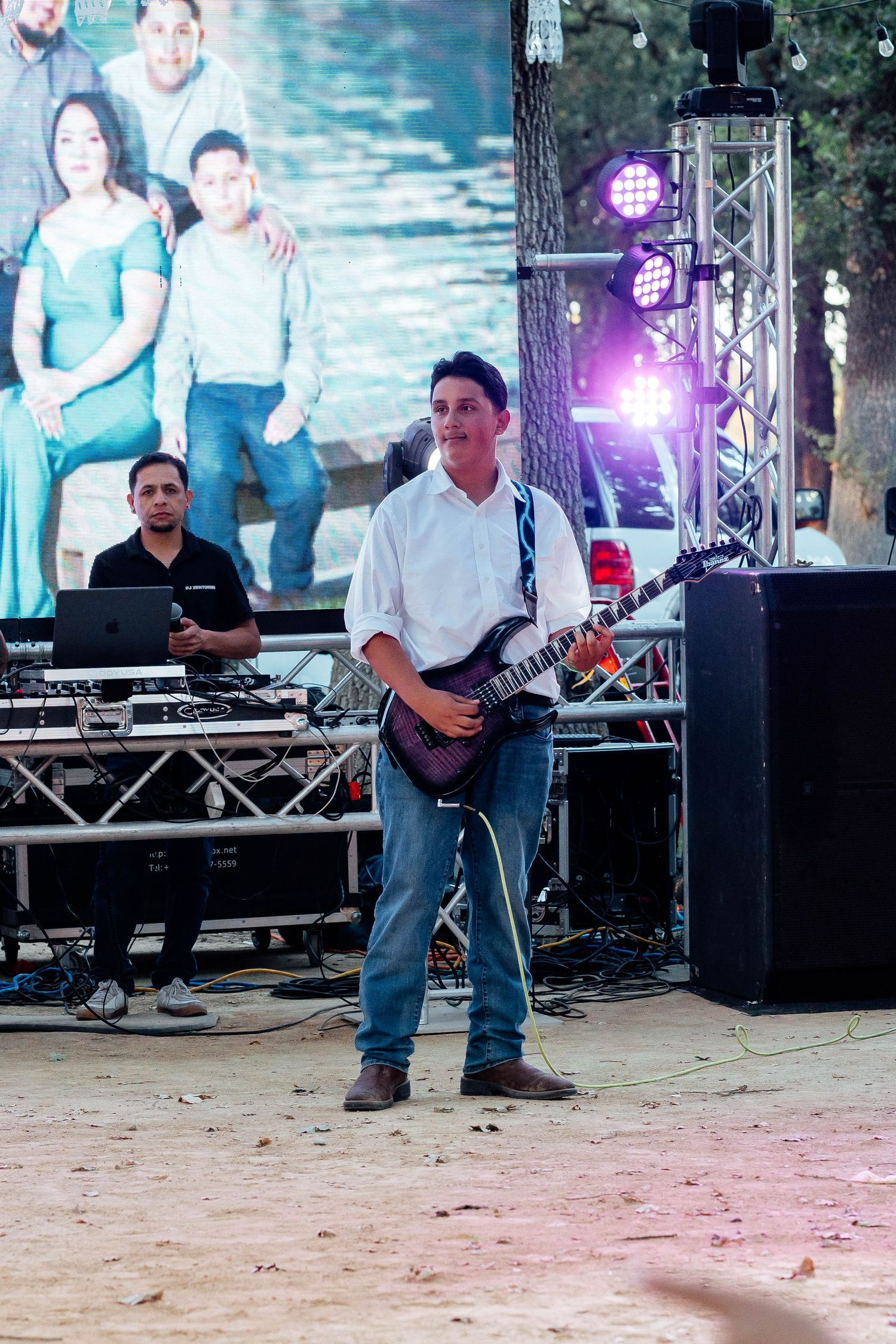 Guitarist in white shirt performing on stage at outdoor wedding reception with keyboard player behind.