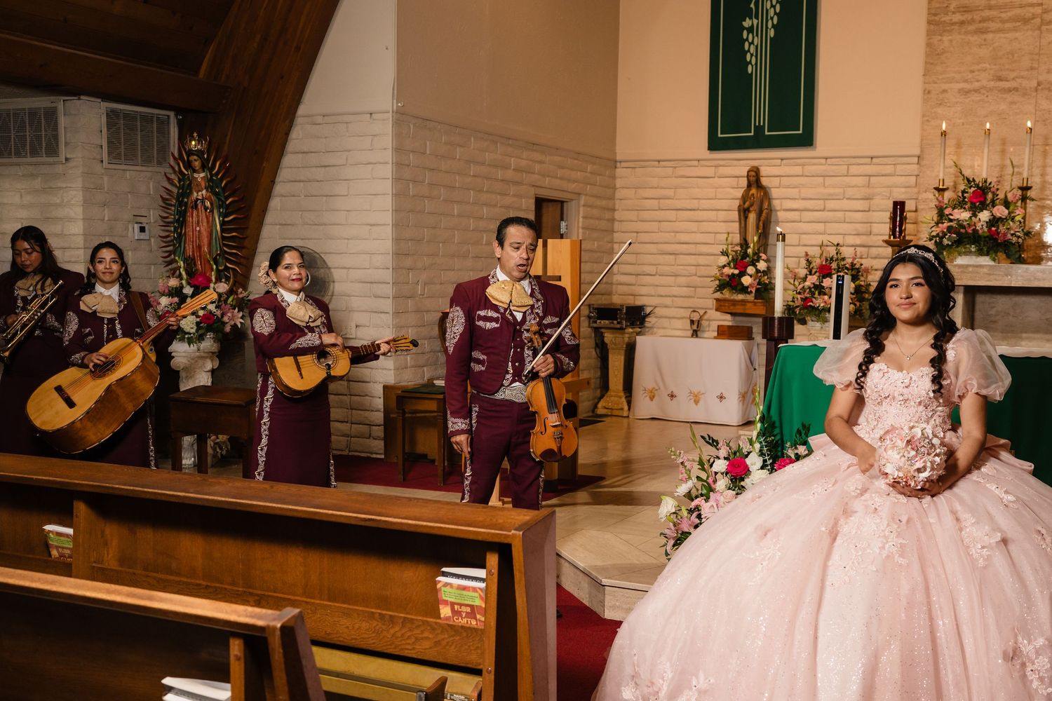 Mariachi band performs at a quinceañera church ceremony while the young woman in a pink ball gown stands nearby.
