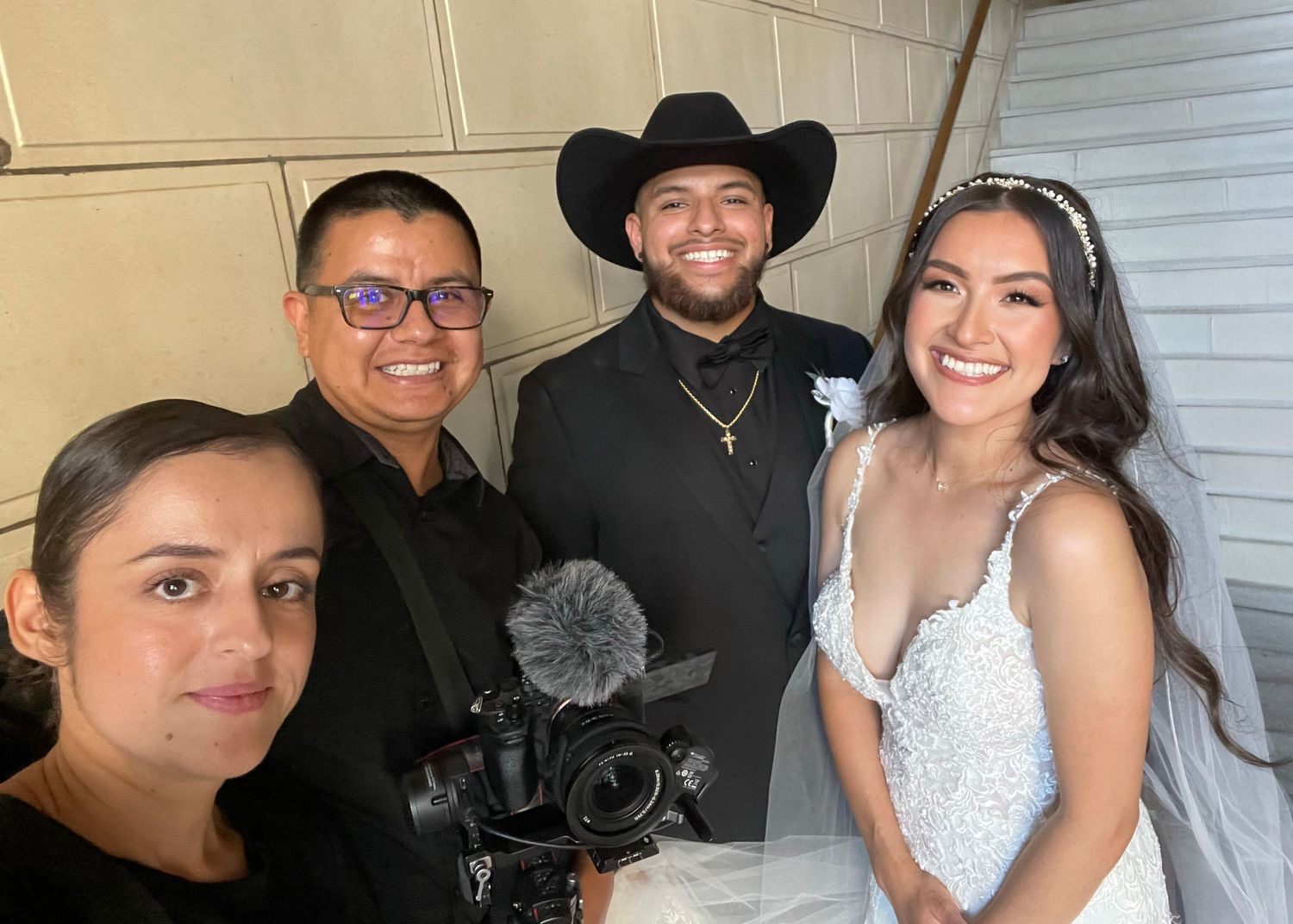 Wedding videographer team poses with bride and groom in cowboy hat at outdoor wedding celebration.