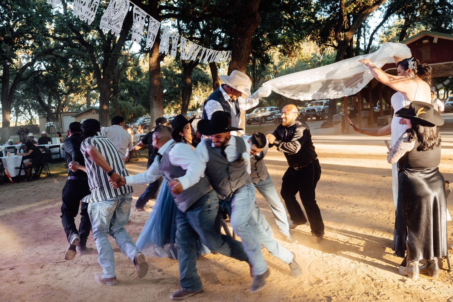 Energetic wedding guests dance and celebrate together on sandy outdoor dance floor at rustic reception.
