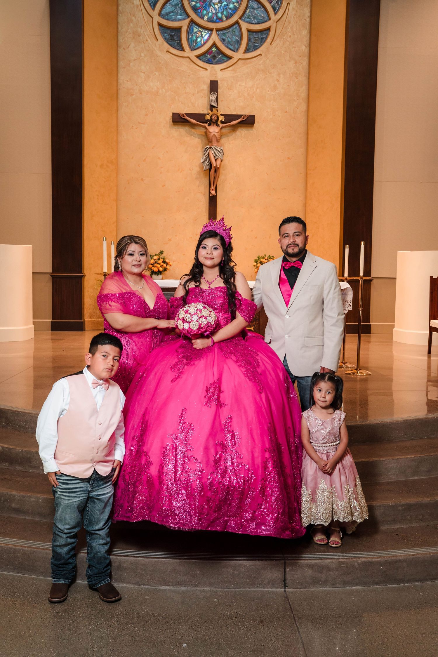 Family poses at church altar during a vibrant hot pink quinceañera celebration with cross backdrop.