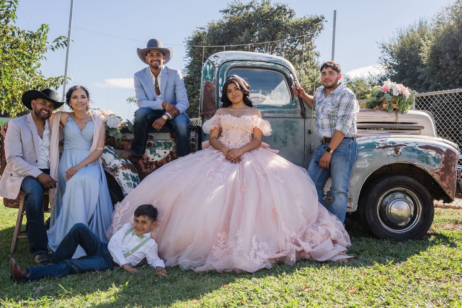 Family poses with quinceañera girl in pink ball gown beside vintage truck outdoors.