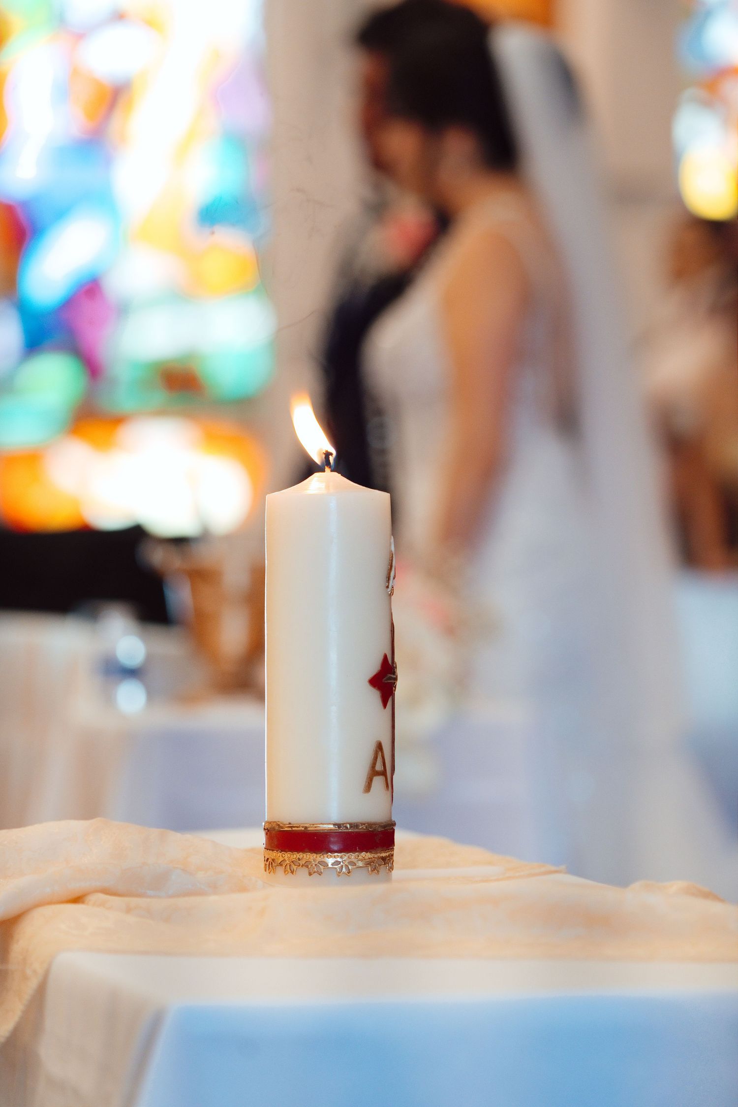Lit unity candle with red cross symbol at a church wedding ceremony with bride in background.