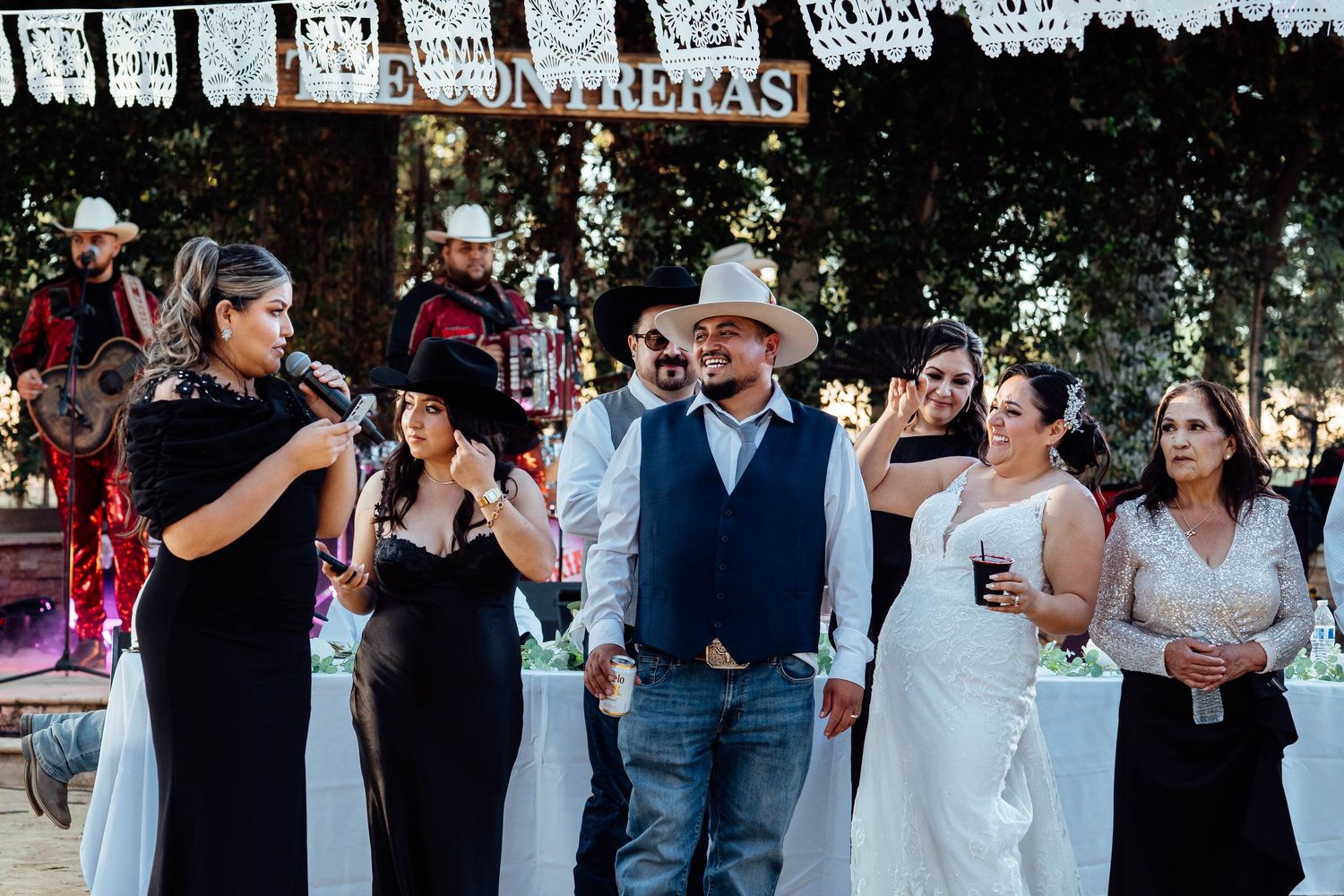 Wedding party gathers near The Contreras sign as a guest gives a toast at outdoor reception.