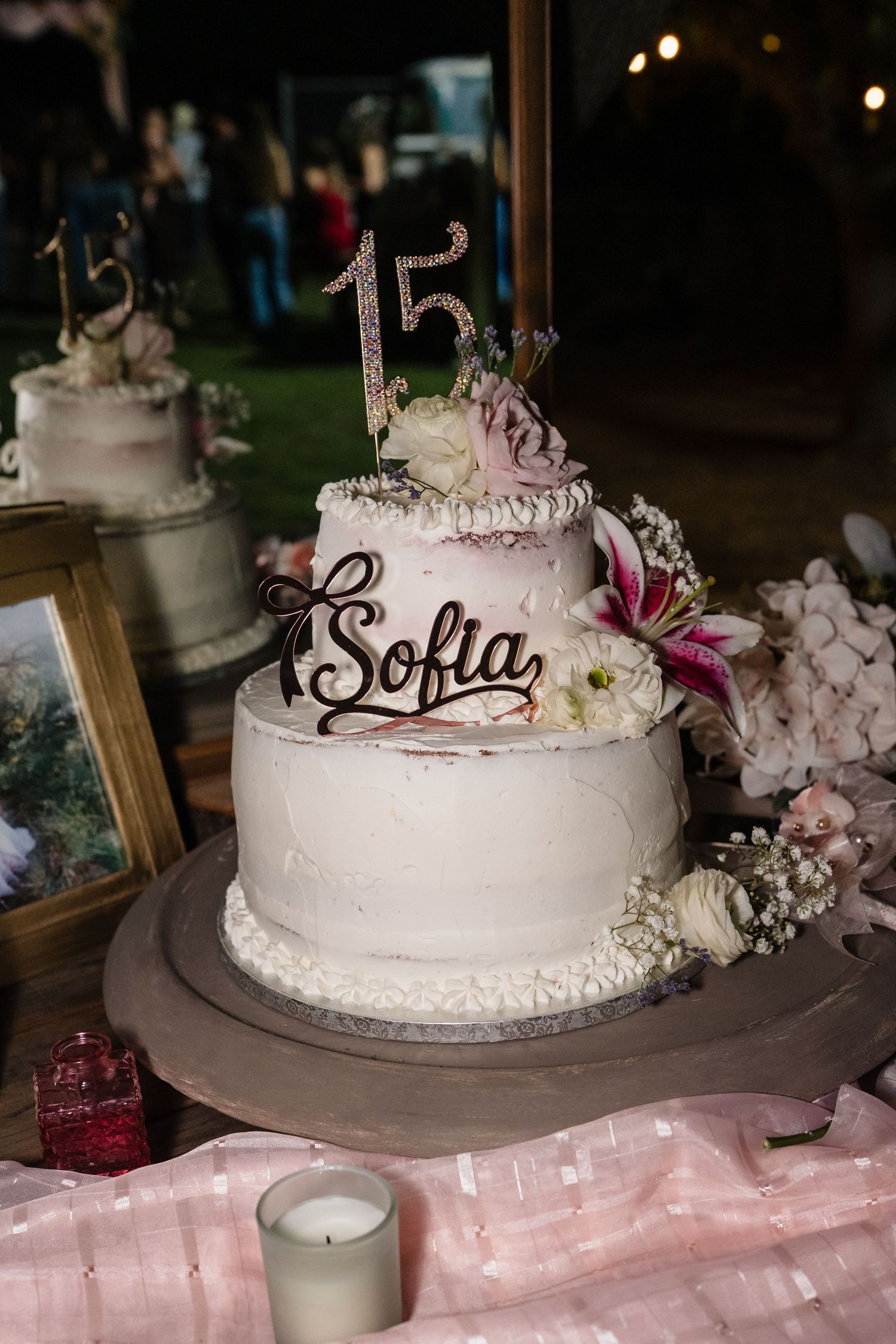 Two-tier white quinceañera cake with Sofia name topper and number 15 decoration with flowers.