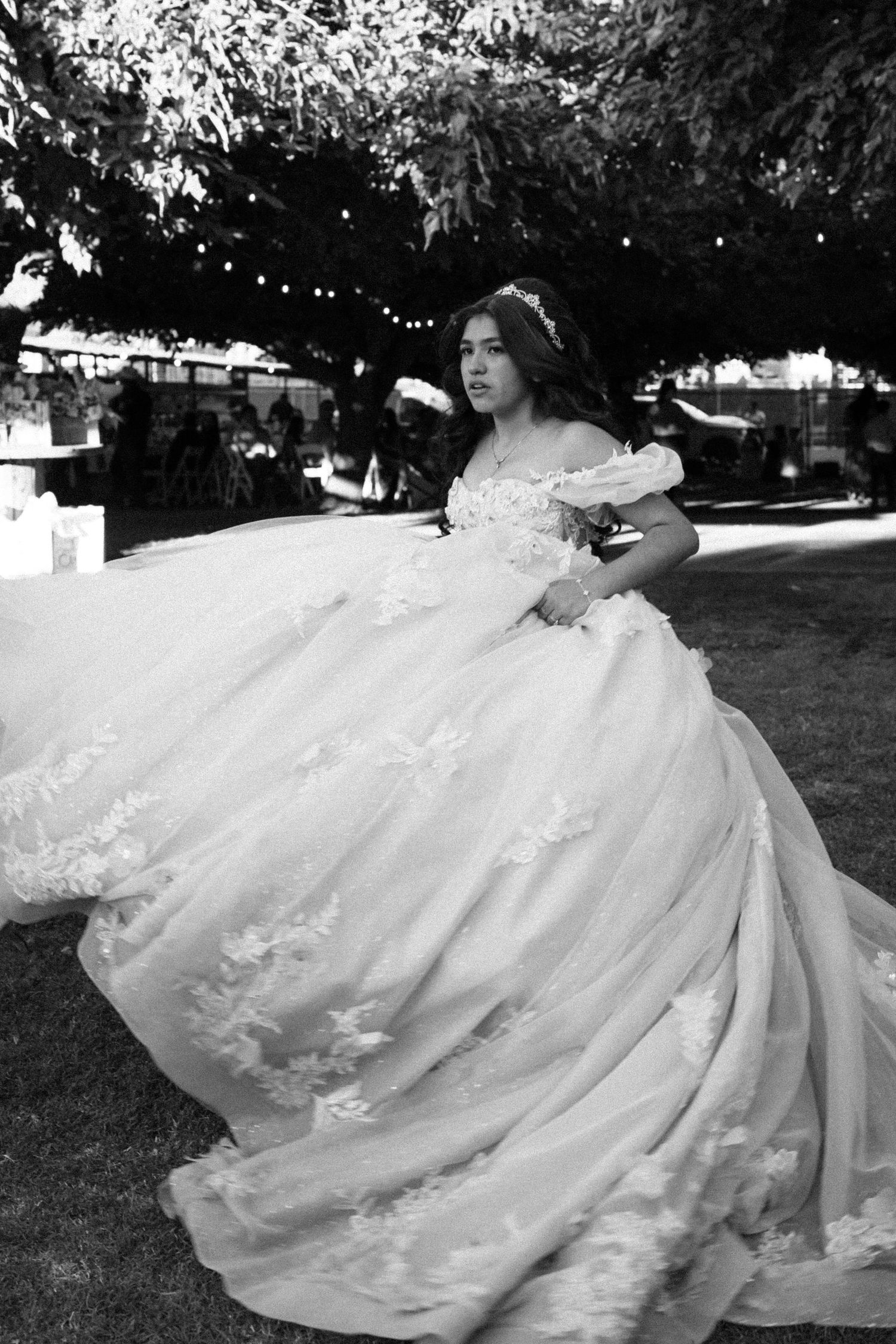 A young woman twirls in an elegant white floral ball gown outdoors in a black and white photo.