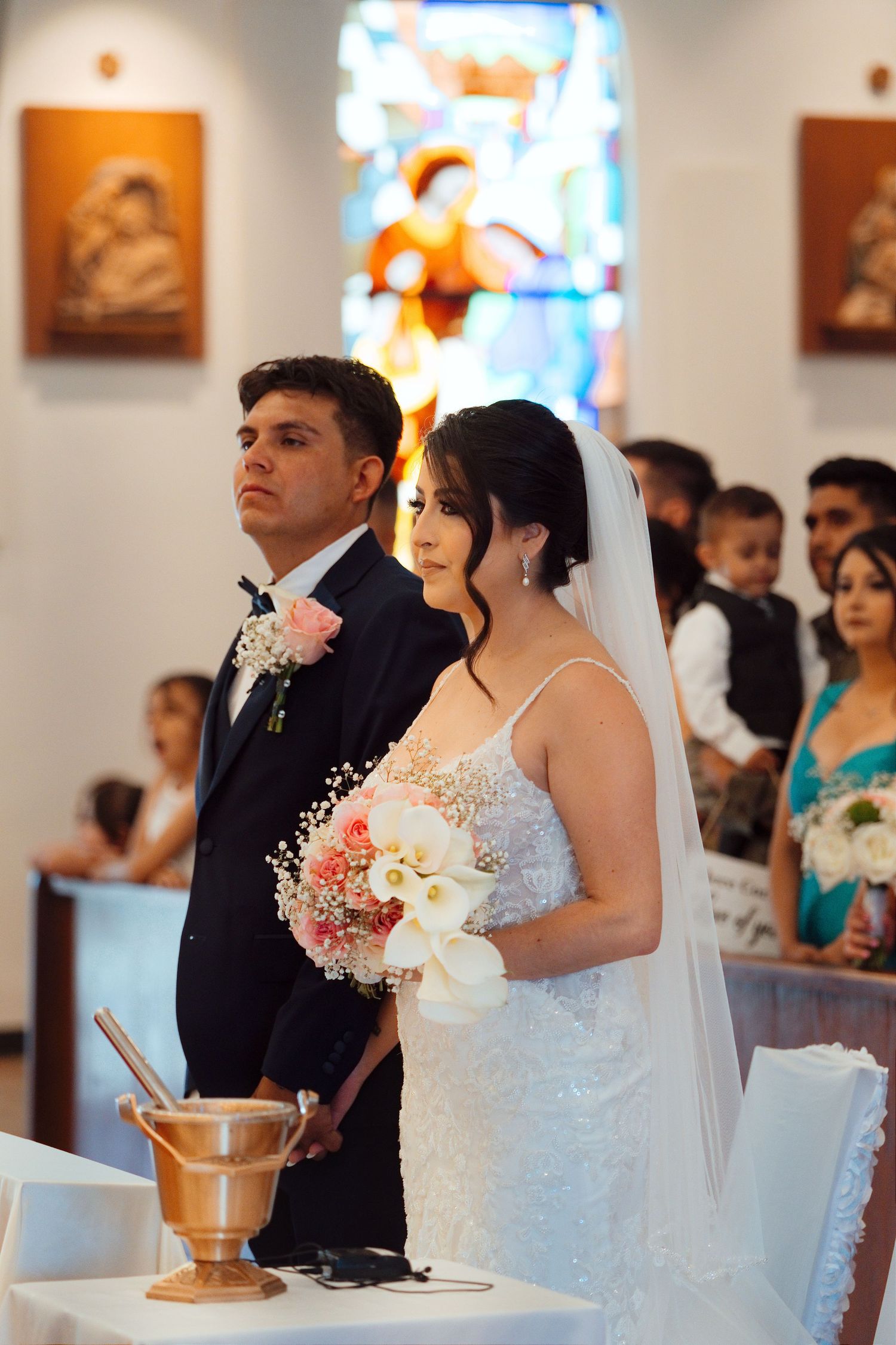 Bride and groom standing at church altar during wedding ceremony, bride holding white floral bouquet with veil.