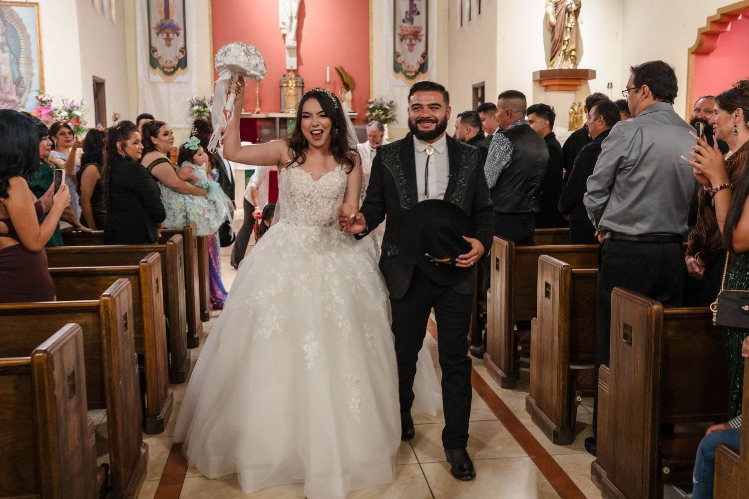 Bride in white ball gown and groom in black suit walk down church aisle after wedding ceremony.