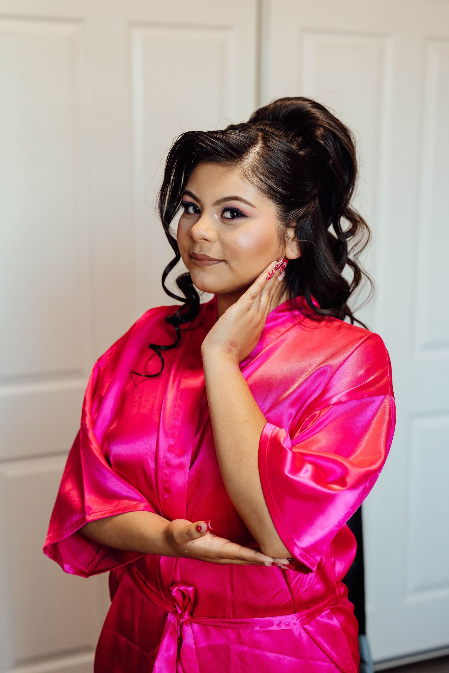 Young woman in a hot pink satin robe poses elegantly while getting ready for her quinceañera celebration.
