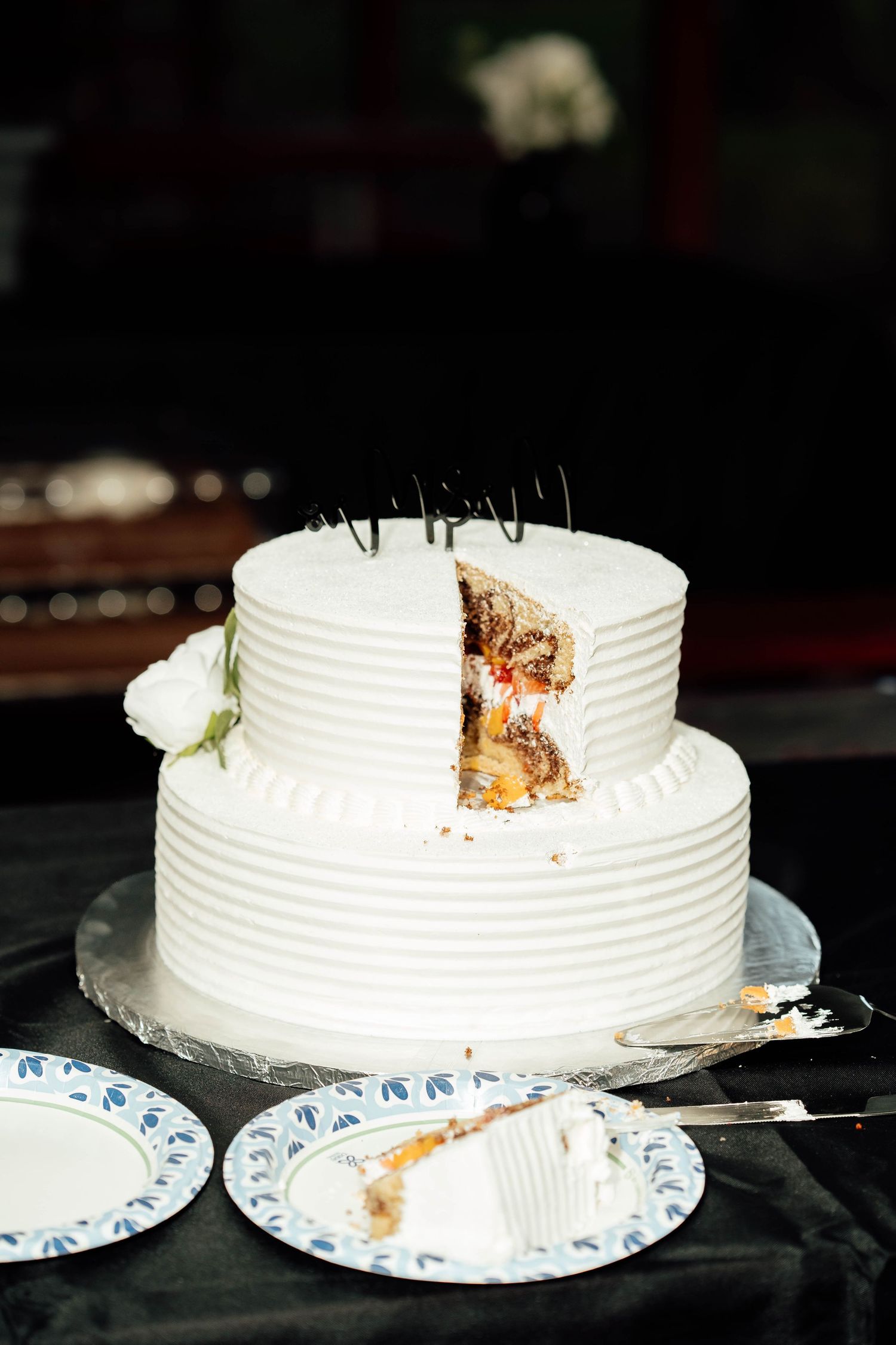 Two-tier white wedding cake with a slice removed revealing chocolate and fruit filling inside.
