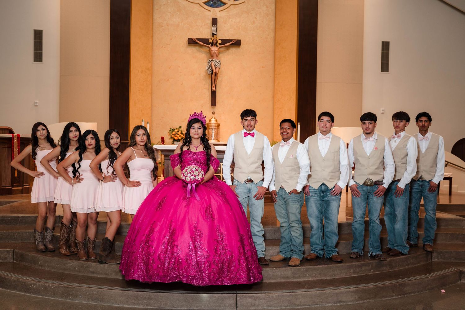 Quinceañera court of honor poses in church with bridesmaids in pink and chambelanes in beige vests.