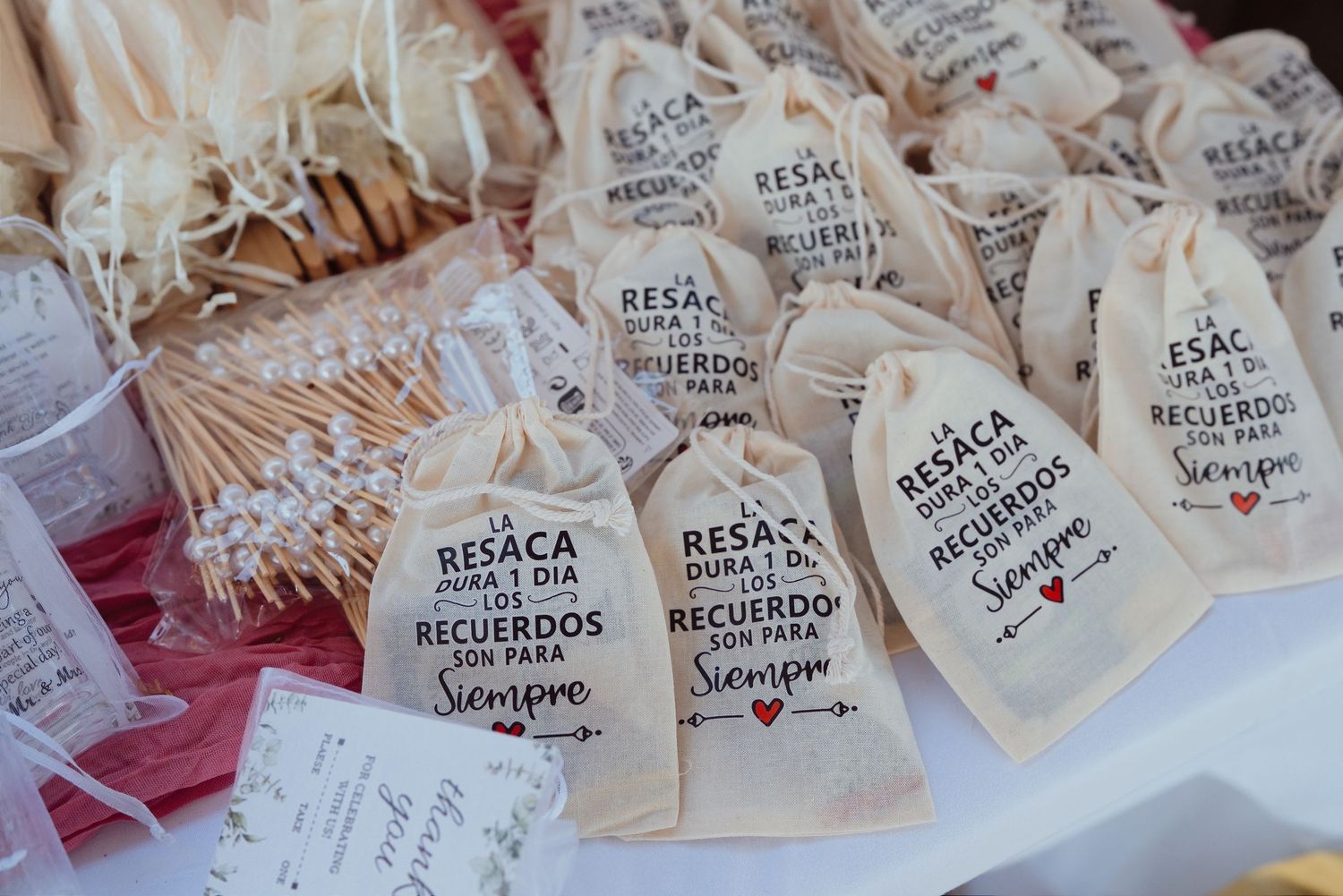 Small burlap wedding favor bags with Spanish text displayed on a table at a wedding reception.