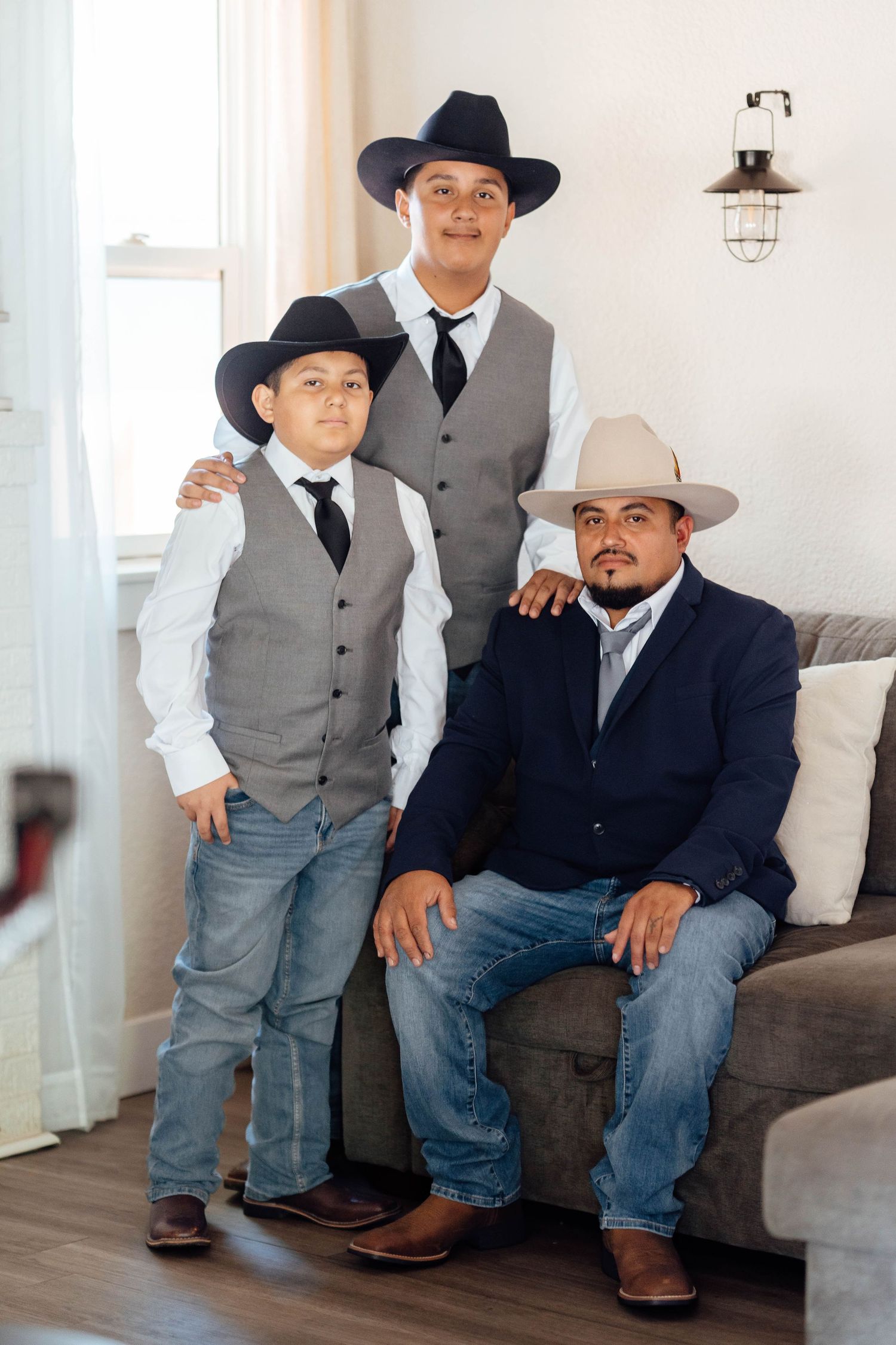 Three males in cowboy hats, vests, and jeans posing together indoors for a formal portrait.