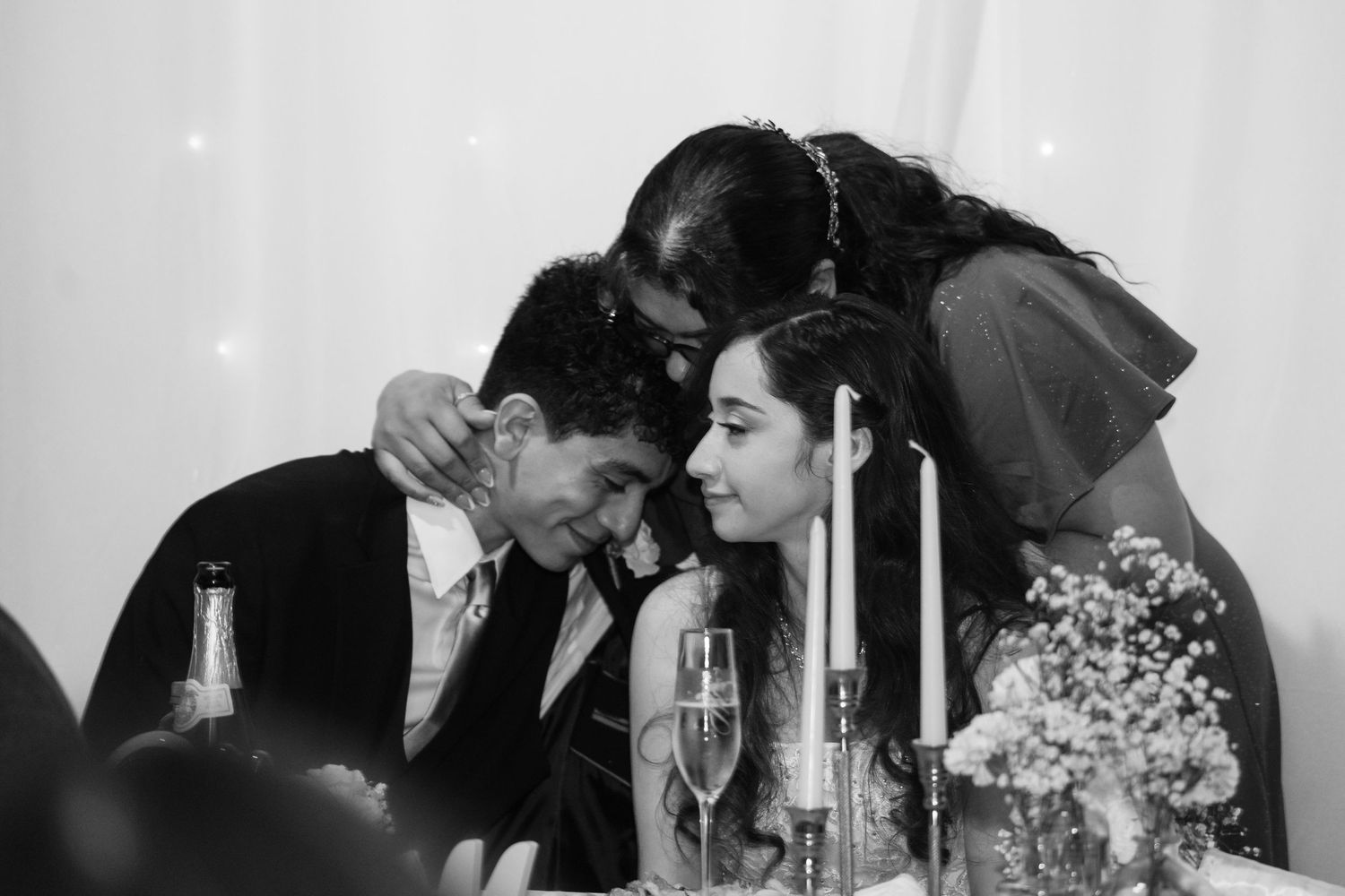 Black and white wedding photo of couple sharing intimate moment at reception dinner table with candles and flowers.