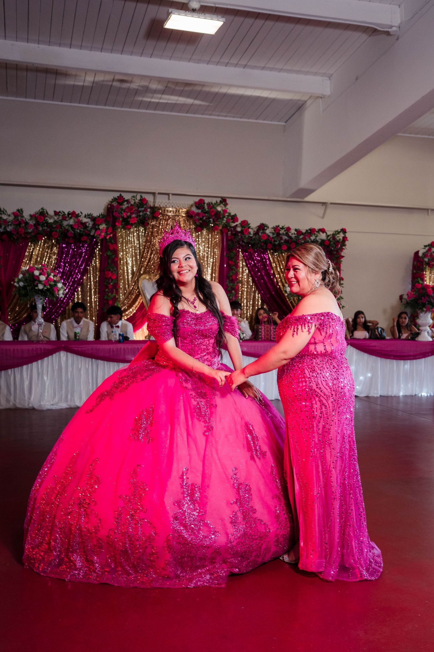 Quinceañera girl and mother share a joyful dance moment in matching hot pink gowns at reception.