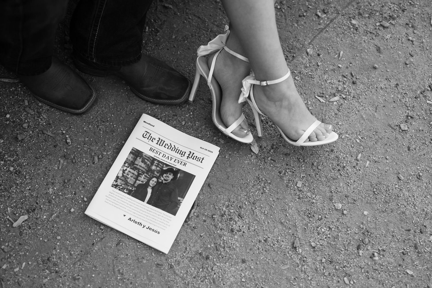 Black and white photo of The Wedding Post newspaper on ground beside cowboy boots and white strappy heels.