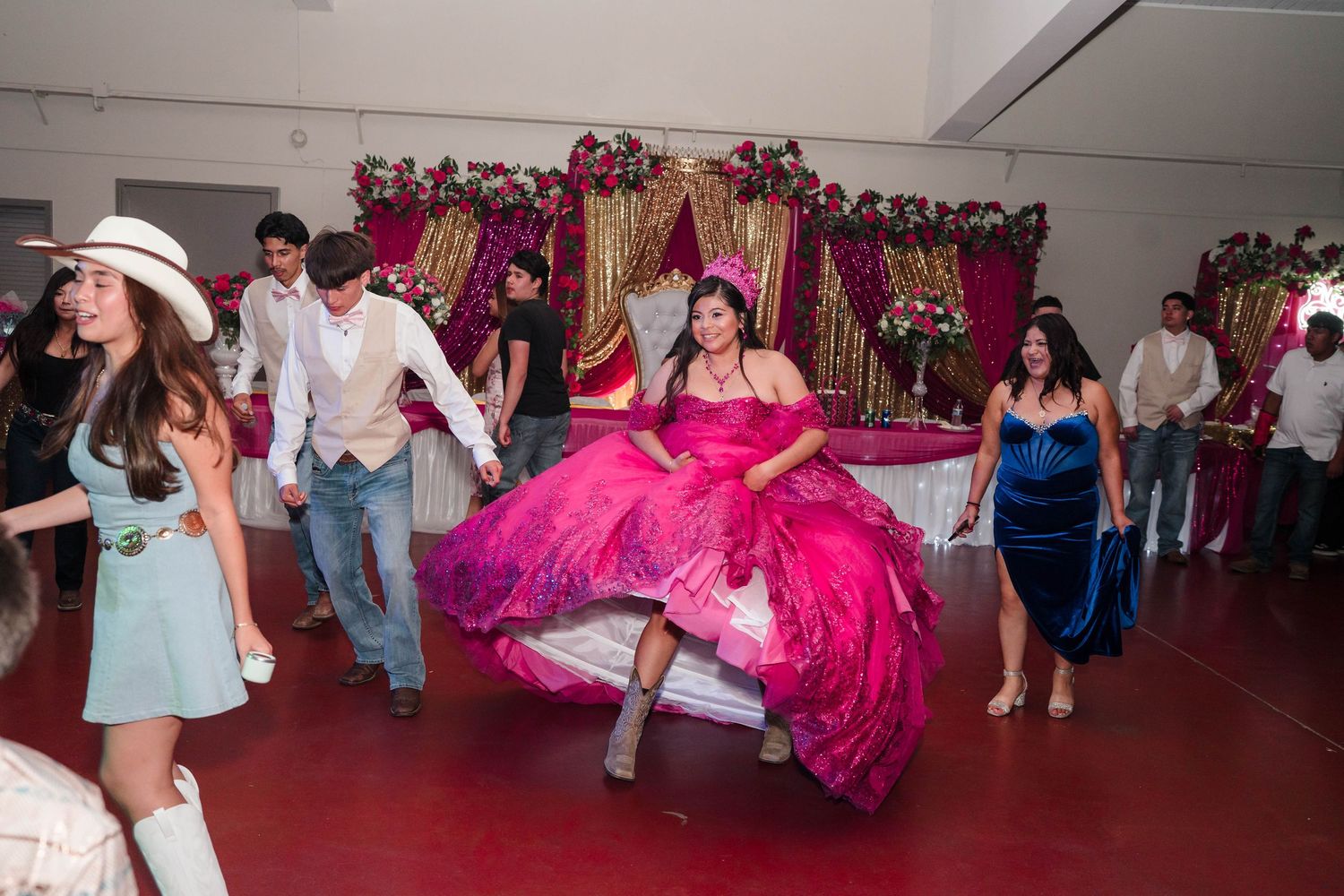 Quinceañera girl in a vibrant pink ball gown dances joyfully with guests on the celebration dance floor.