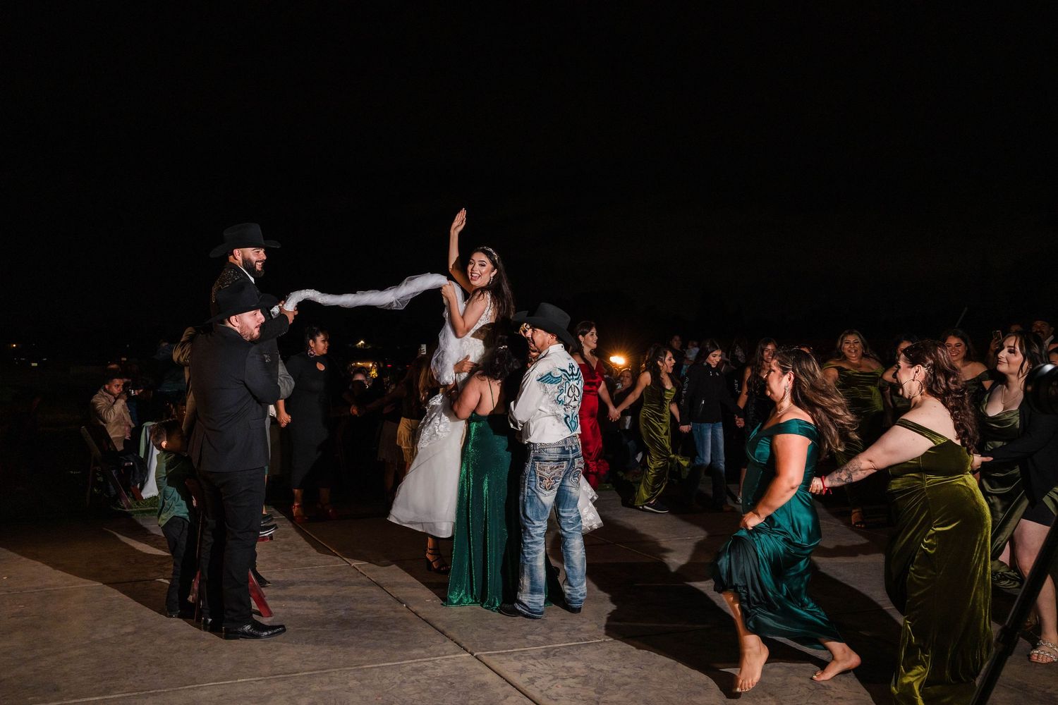 Bride in white wedding gown celebrates with guests during lively outdoor nighttime wedding reception dance party.