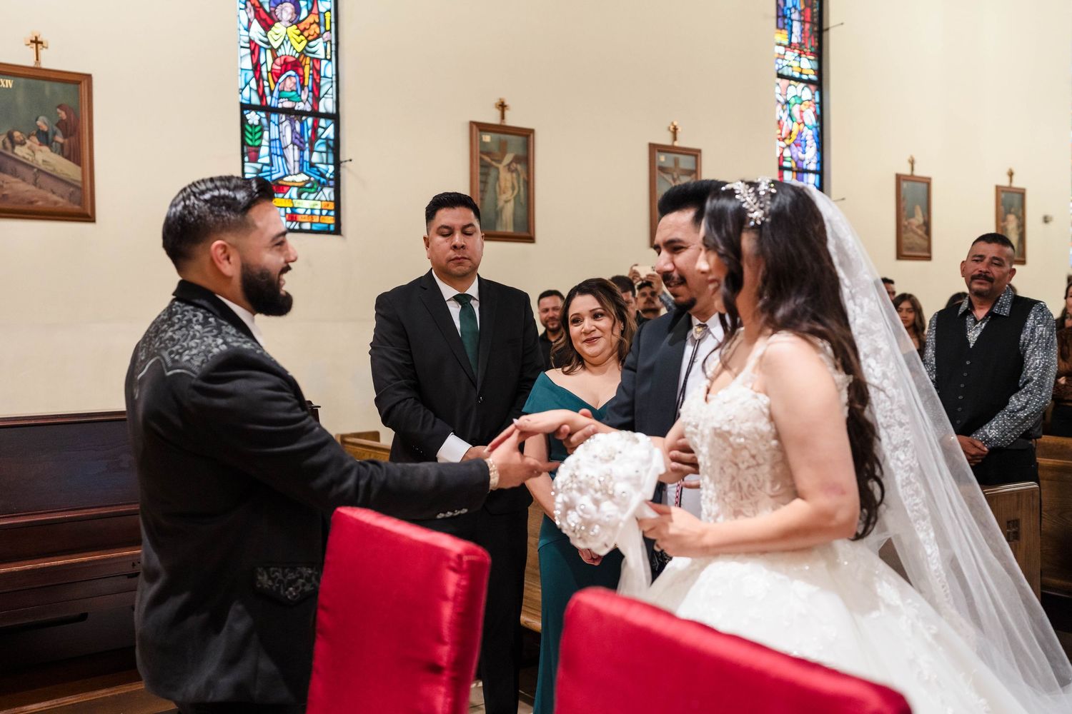 Bride and groom exchange rings during a church wedding ceremony with guests watching in the background.