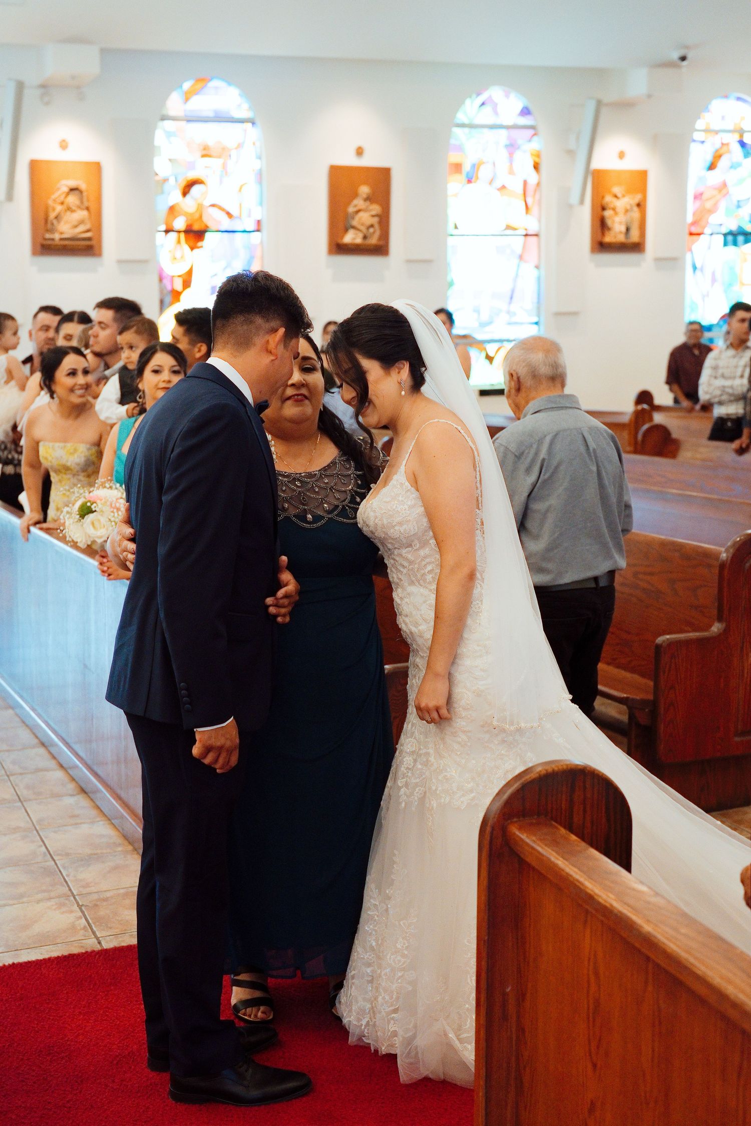 Bride and groom share a tender moment with family member at church altar during wedding ceremony.