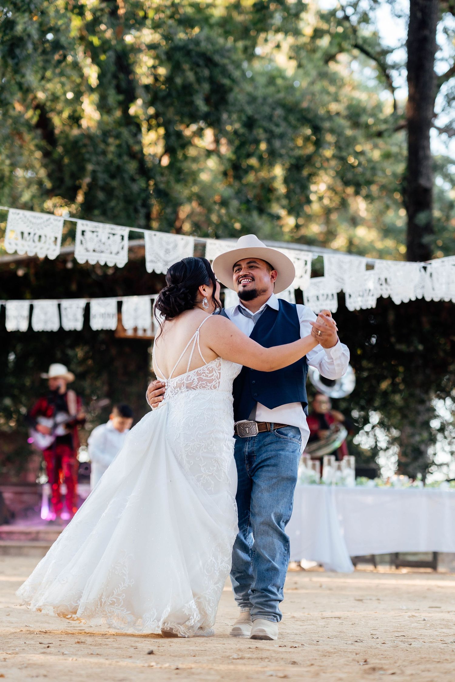 Bride and groom share first dance under papel picado banners at a rustic outdoor wedding reception.